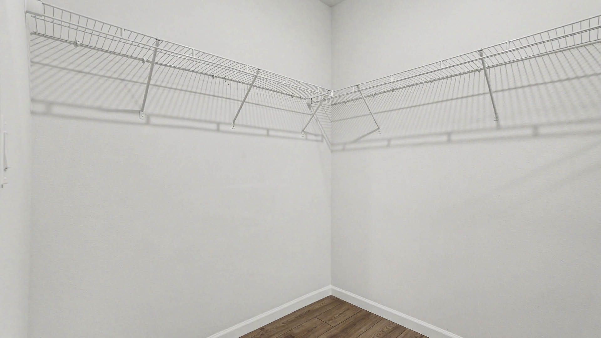 A spacious, walk-in closet with white wire shelves against a light-colored wall.