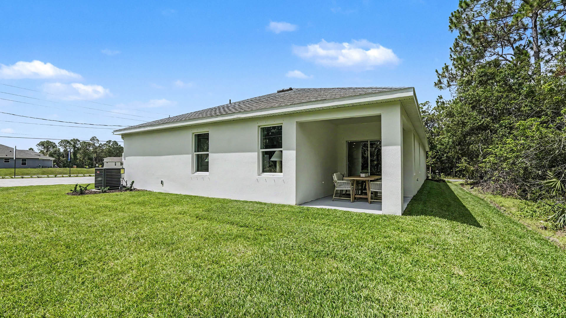 A rear view of a house featuring a stucco exterior, sliding glass door, and a covered patio.