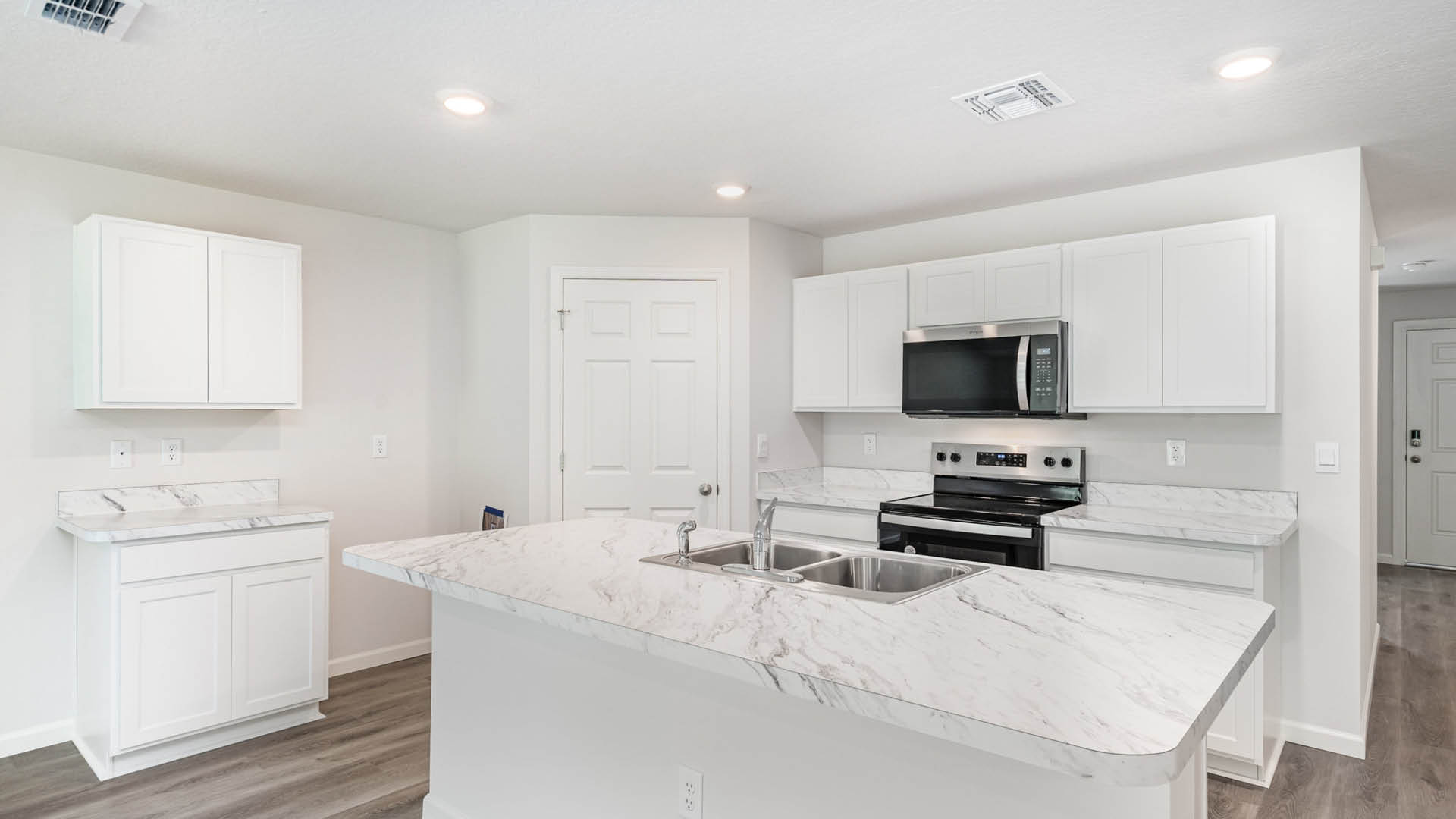 A large kitchen with stainless steel appliances and a center island. An entryway hallway leading to the front door is visible.