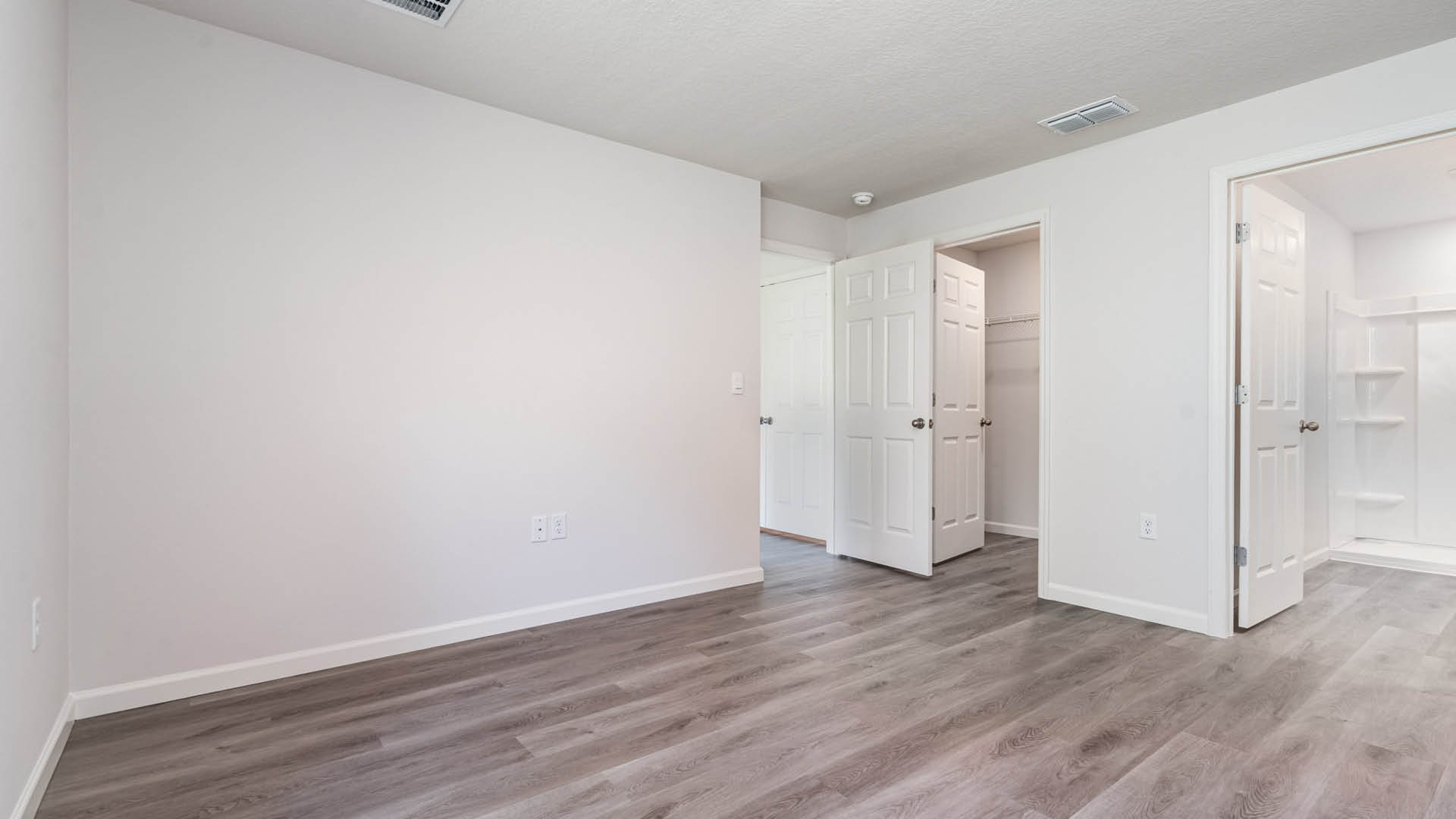 A large bedroom with an open door leading to another area, a walk-in closet, and an open door leading to an ensuite bathroom.