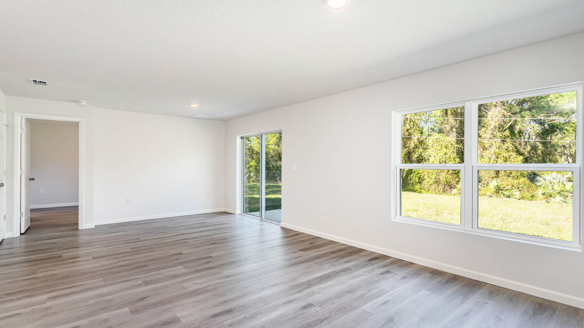A bright living area featuring large windows and a sliding glass door leading to a green outdoor area.