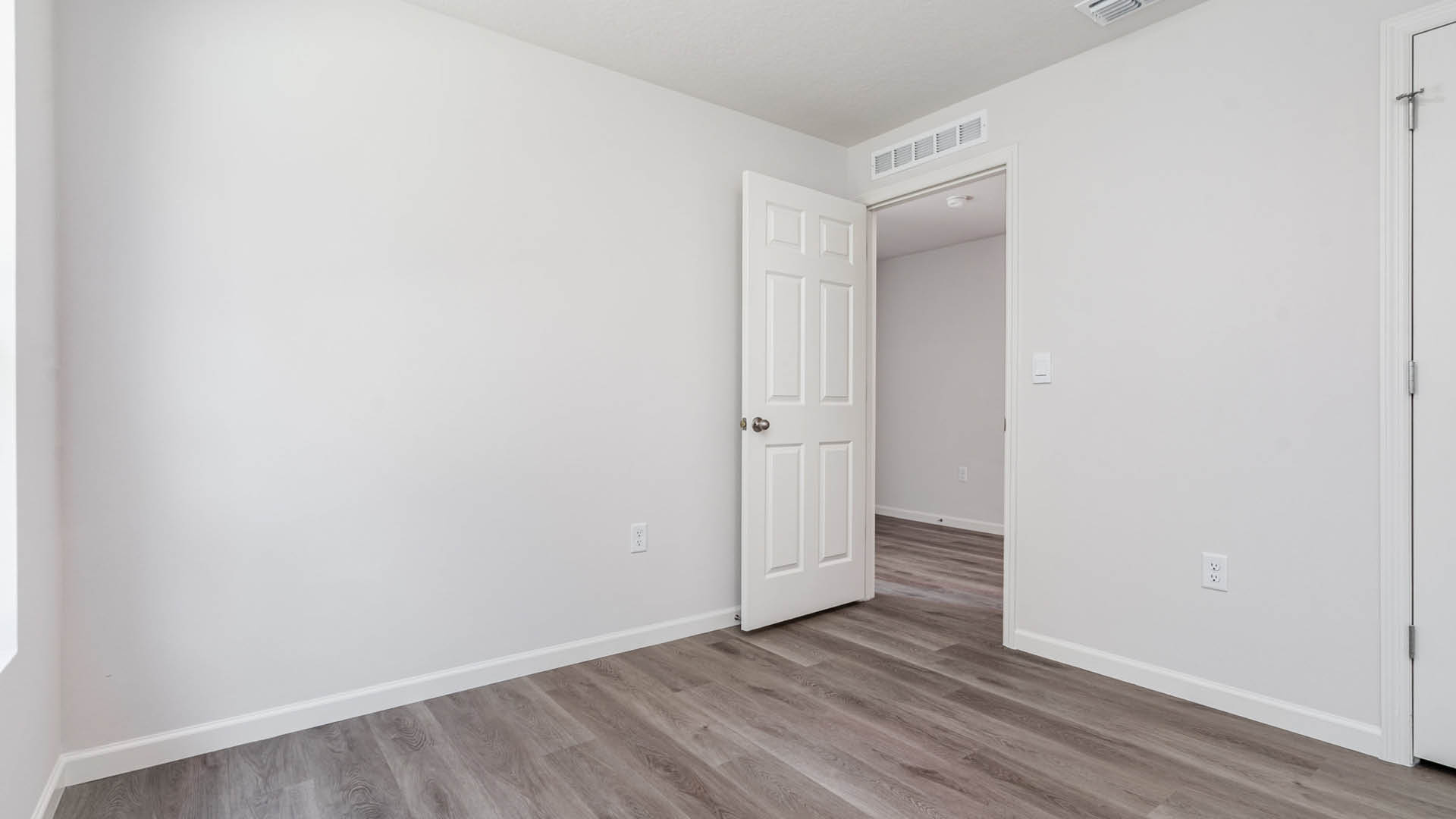 A large bedroom with an open door leading to another area.