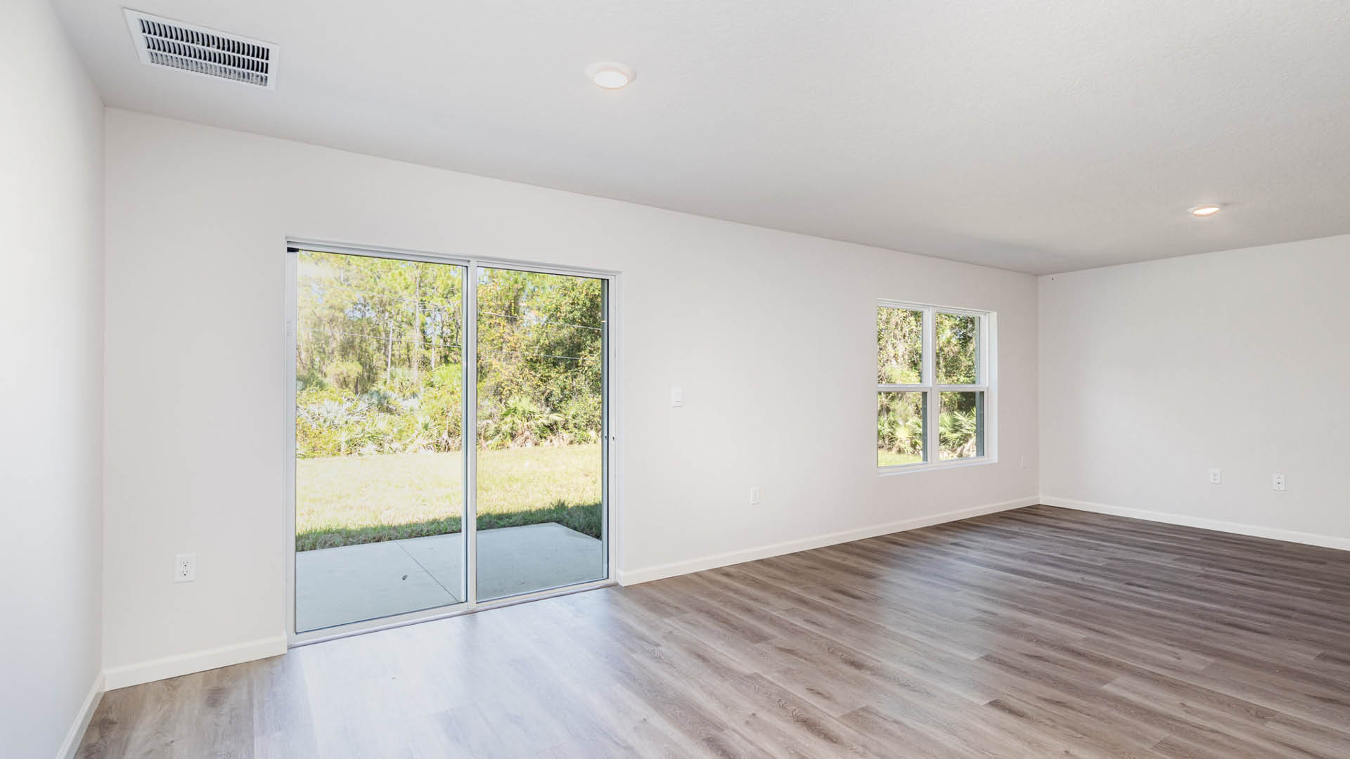 A bright living area featuring large windows and a sliding glass door leading to a green outdoor area.