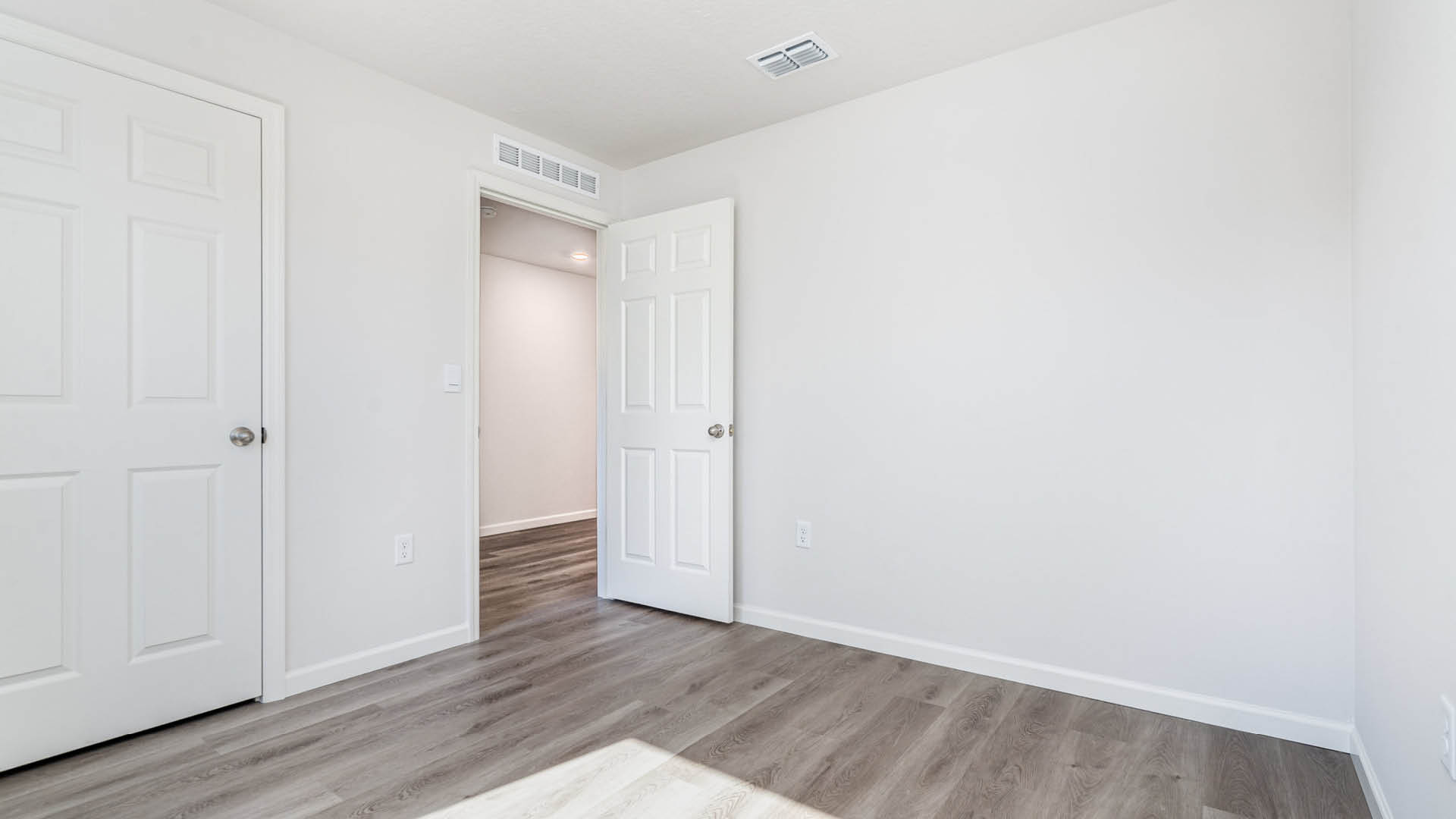 A large bedroom with an open door leading to another area and a closed closet door.
