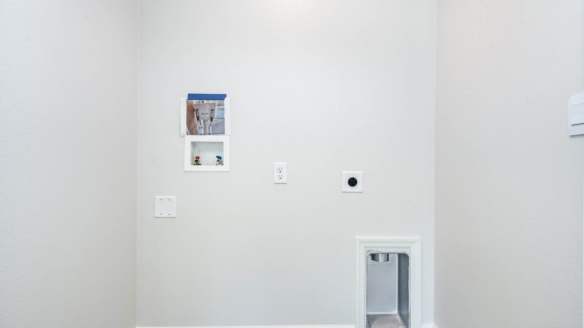 A laundry room with utility connections on the wall.