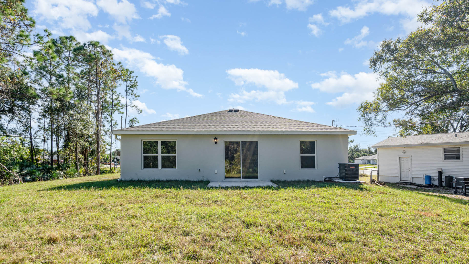Rear view of a house featuring a white stucco exterior, sliding glass door, and a well-kept lawn with a small shrub.