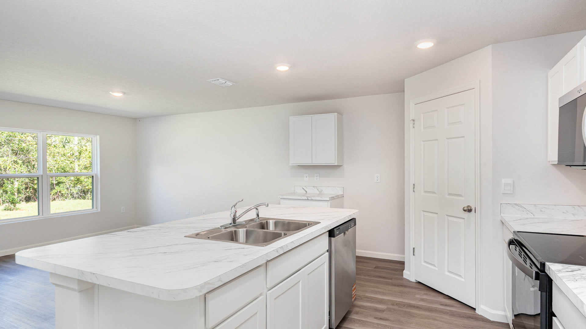 A large kitchen with stainless steel appliances and a center island with seating. A large window lets in natural light onto a dining area.