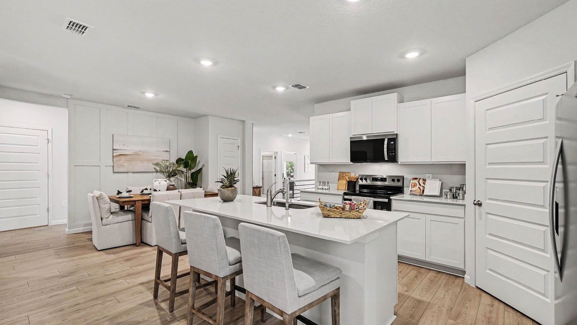 A large kitchen with stainless steel appliances and an island with seating. A dining area and several doors to other rooms are visible.