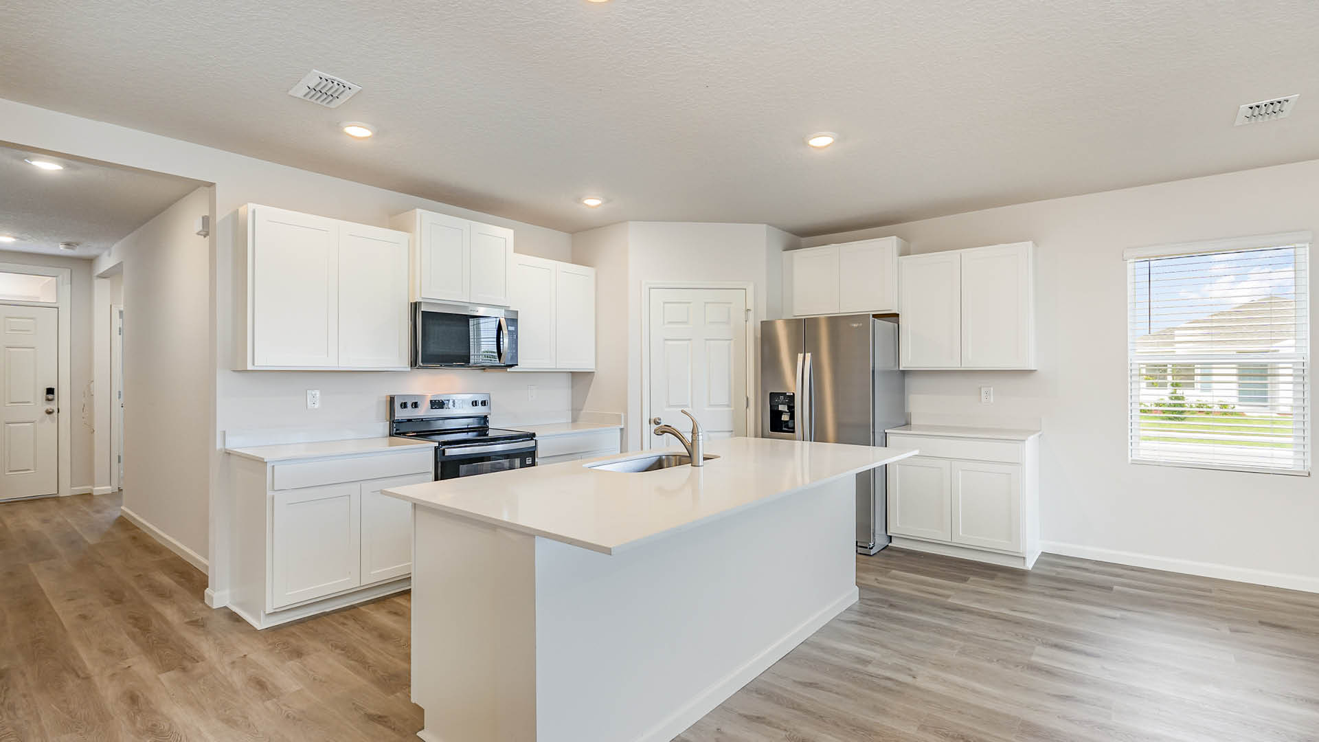 A large kitchen with quartz countertops, stainless steel appliances, and an island. An entryway hallway leading to the front door is visible.