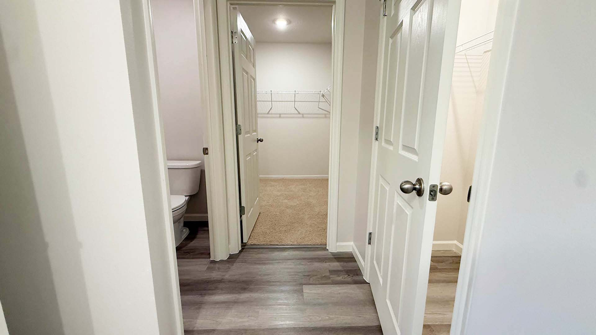 A hallway featuring a door to a toilet on one side and a closet on the opposite side.