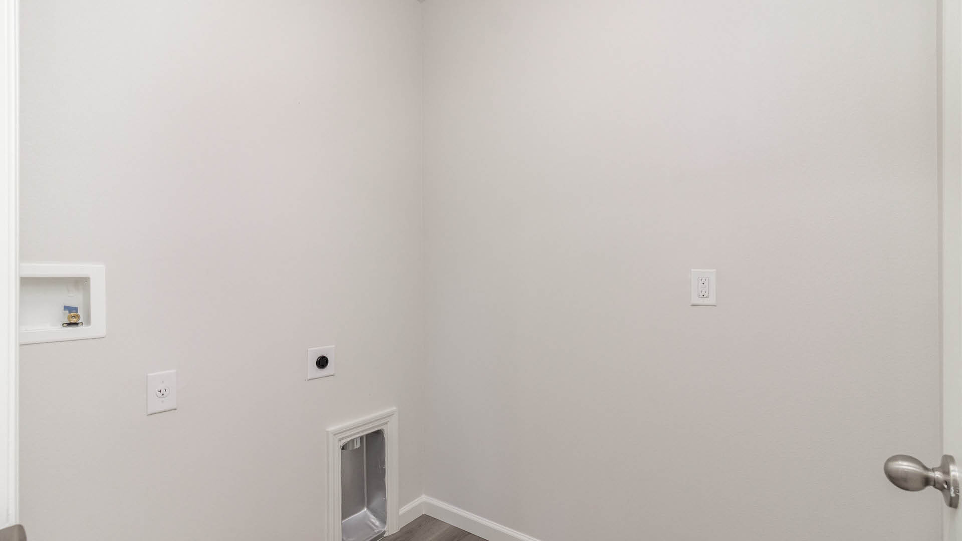A laundry room with utility connections on the wall and Mohawk® Revwood Select Plank Flooring.