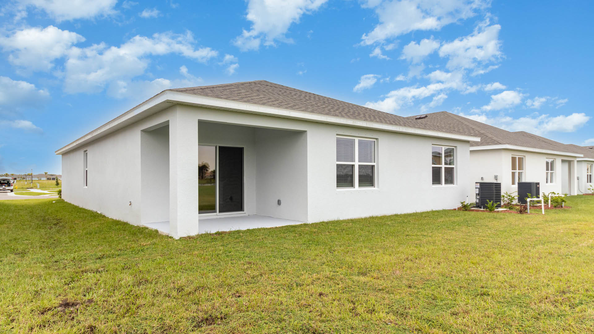 A rear view of a house featuring a stucco exterior, sliding glass door, and a covered patio.