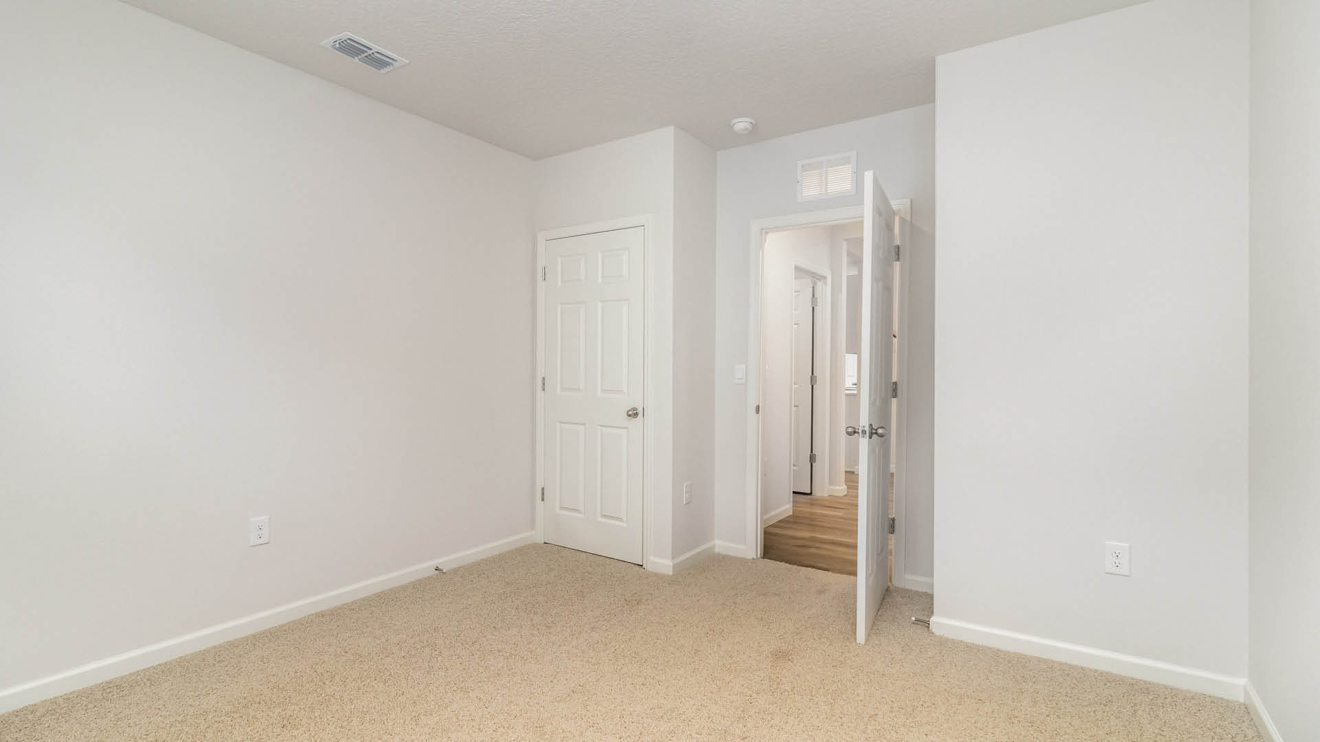 An empty room with beige carpet and white walls. The door to the room is open, while another door, leading to the closet, is closed.