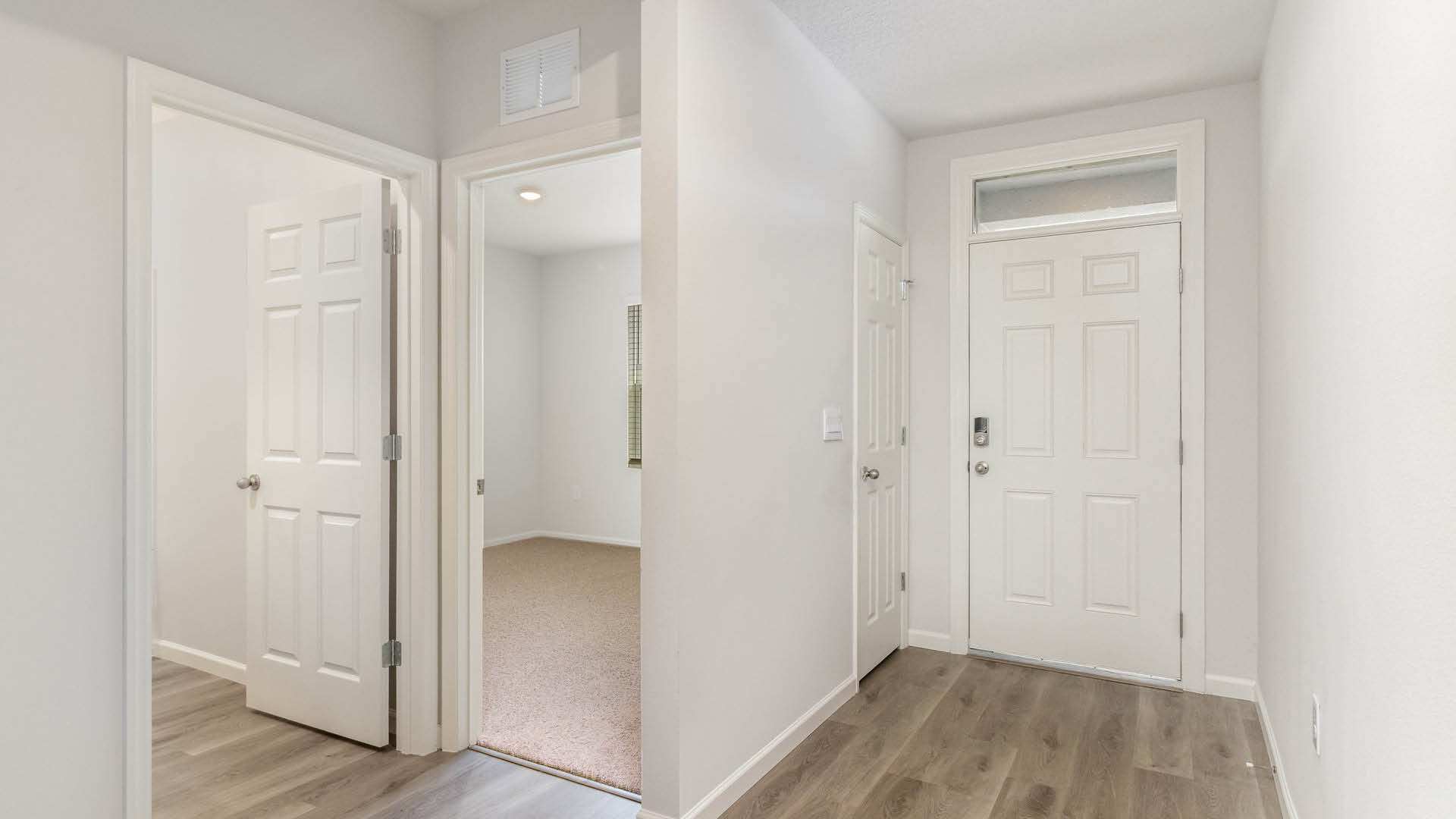 A bright entryway hallway with Mohawk® Revwood Select Plank Flooring, featuring a closed front door and two open doors leading elsewhere.