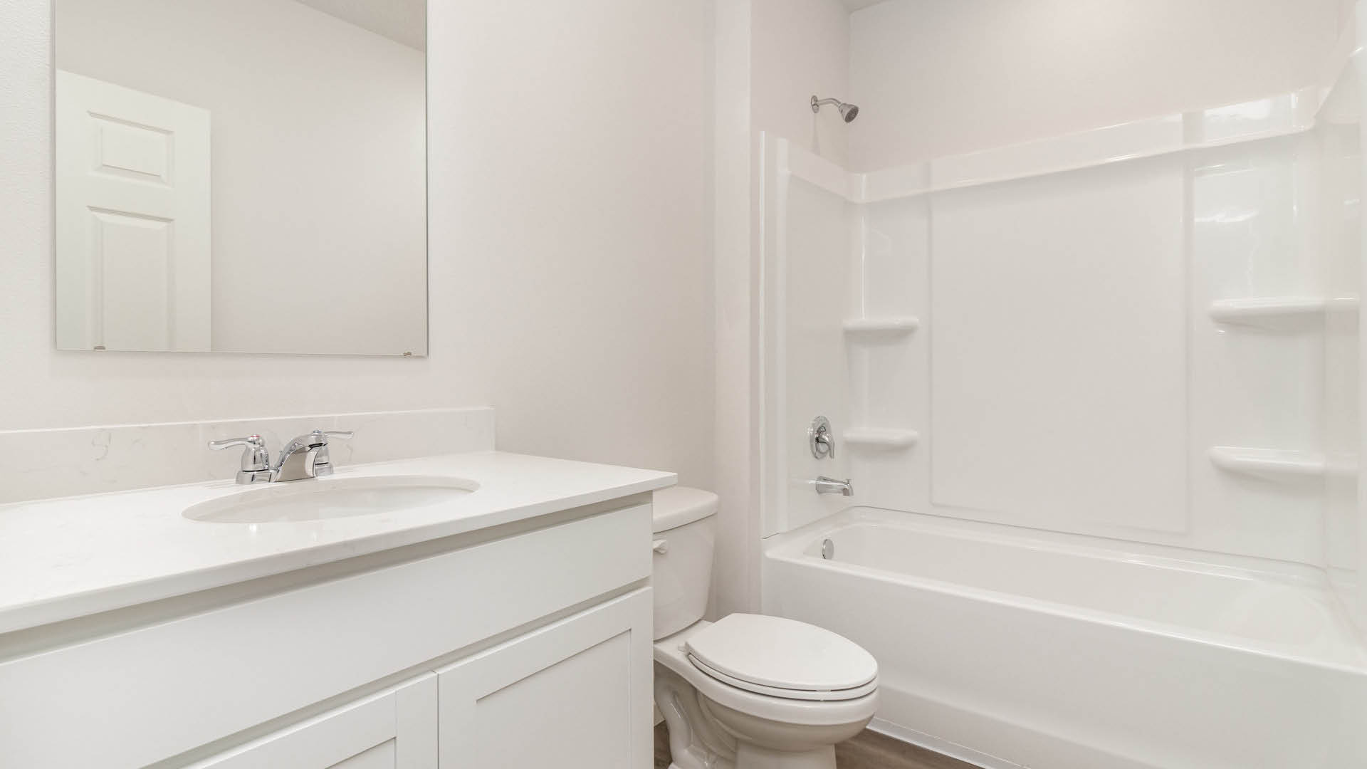 A clean, modern bathroom featuring quartz countertops, a bathtub with a shower, and a large mirror against neutral-colored walls.