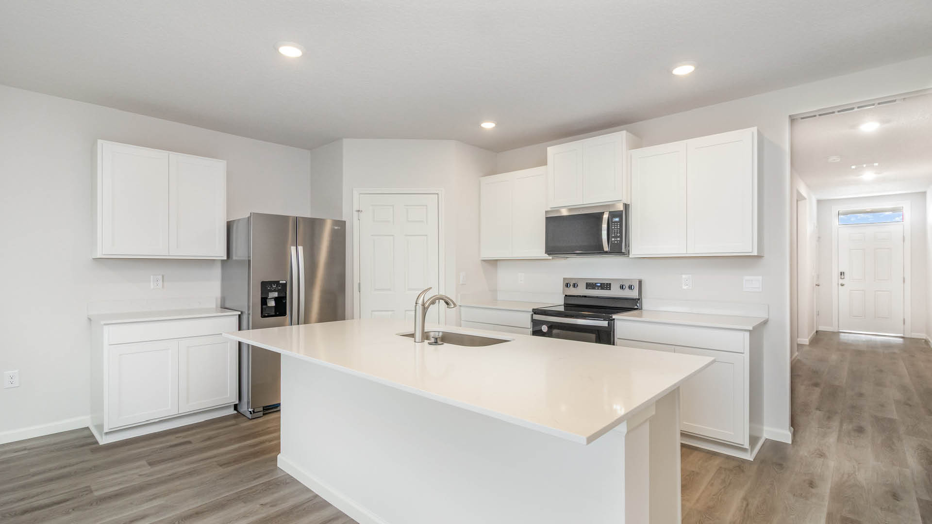 A modern kitchen with white cabinetry, stainless steel appliances, and a large island. Bright and welcoming entryway visible.
