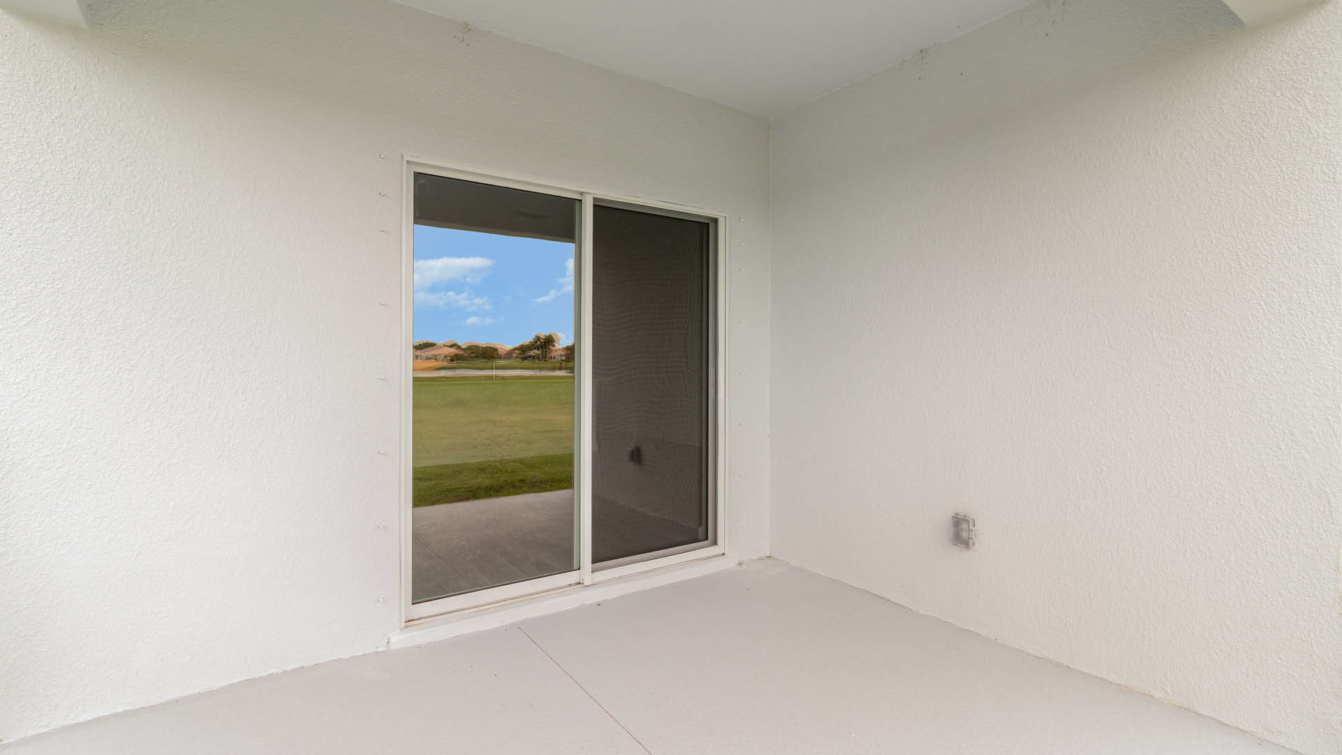 A rear view of a house featuring a stucco exterior, sliding glass door, and a covered patio.
