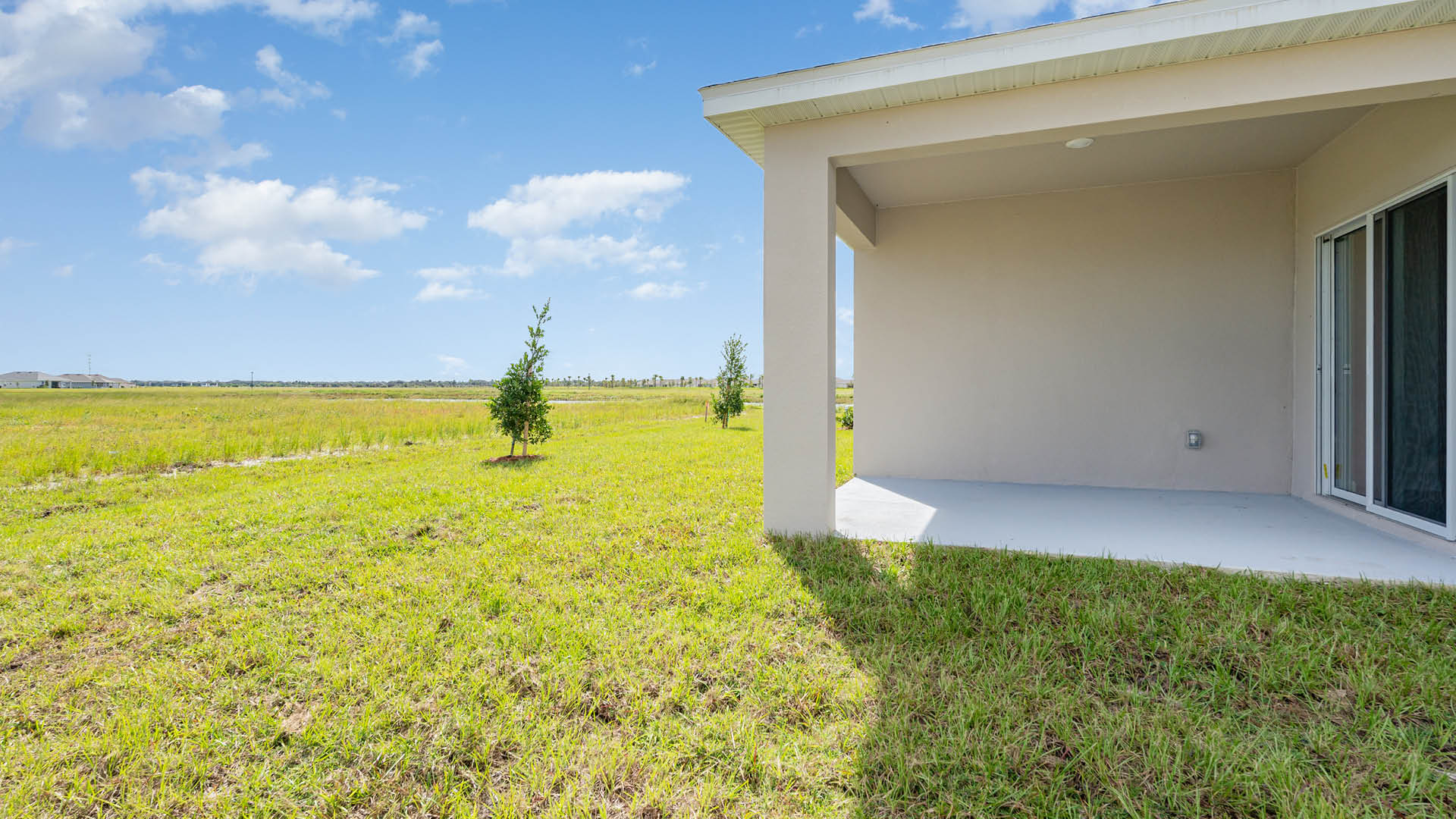 A rear view of a house featuring a stucco exterior, sliding glass door, and a covered patio.