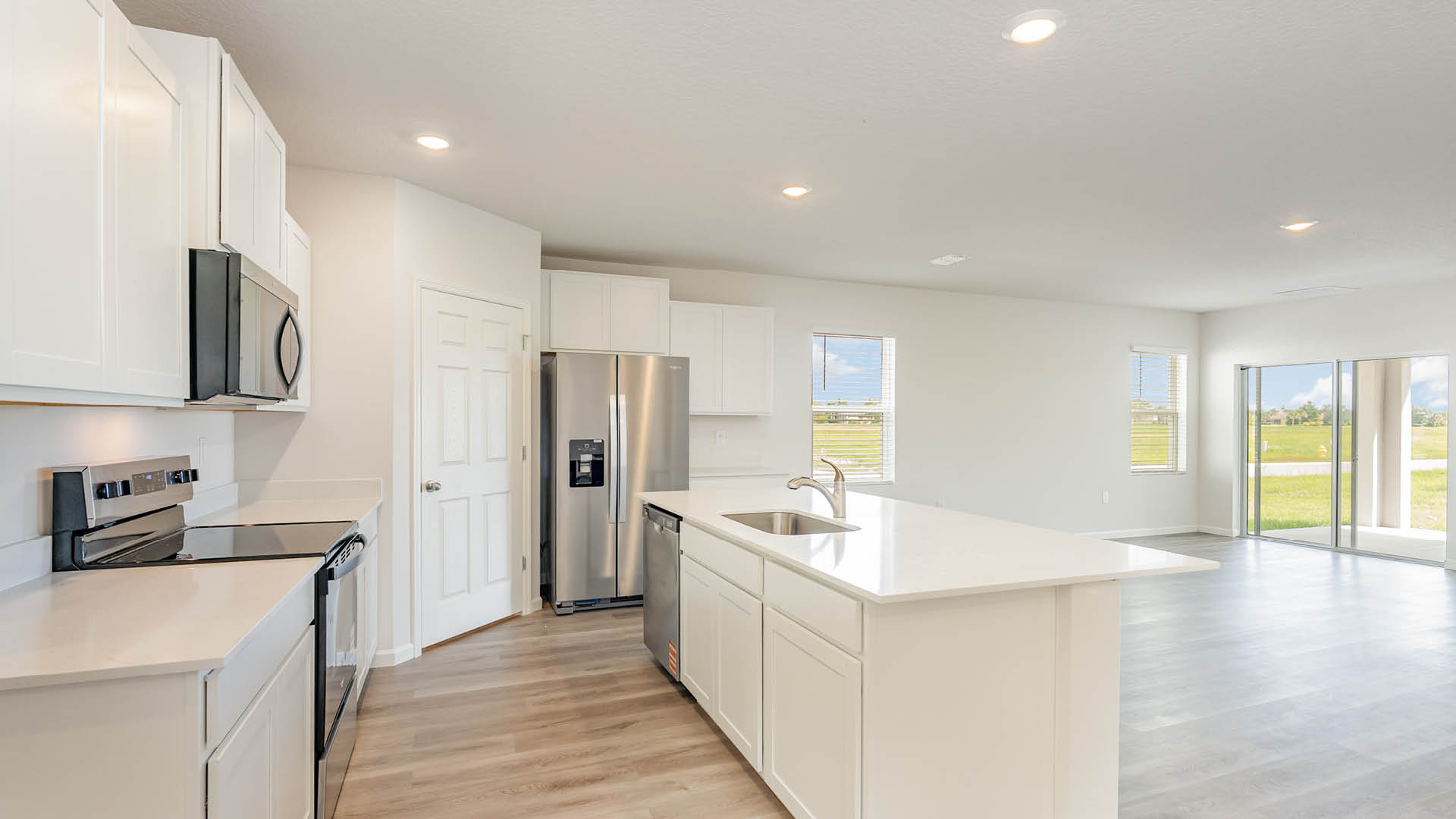 large kitchen with quartz countertops, stainless steel appliances, and an island. A dining area featuring large windows and a sliding glass door are visible.