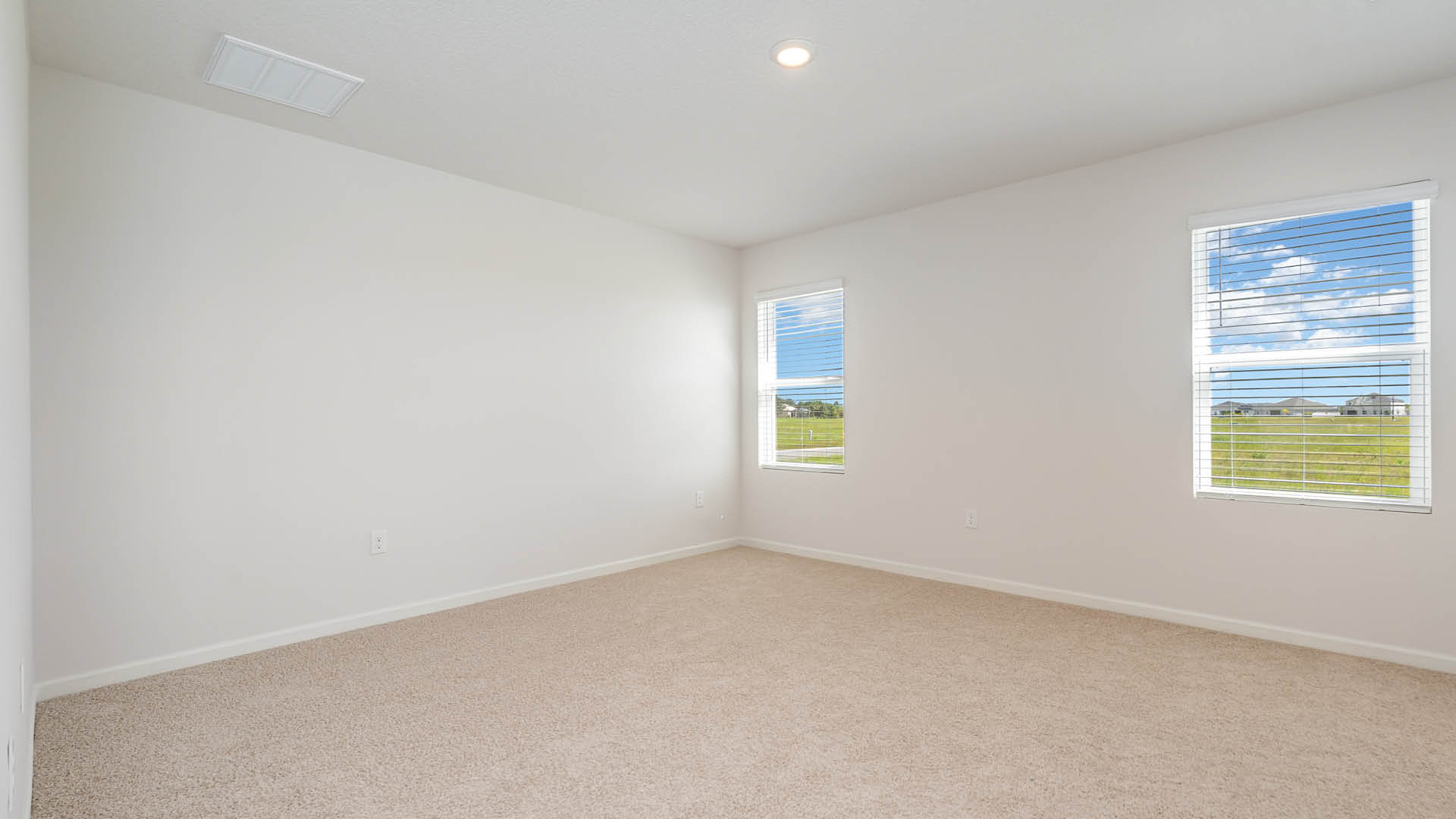 A large bedroom with beige carpet, white walls, and two windows, allowing natural light to illuminate the space.