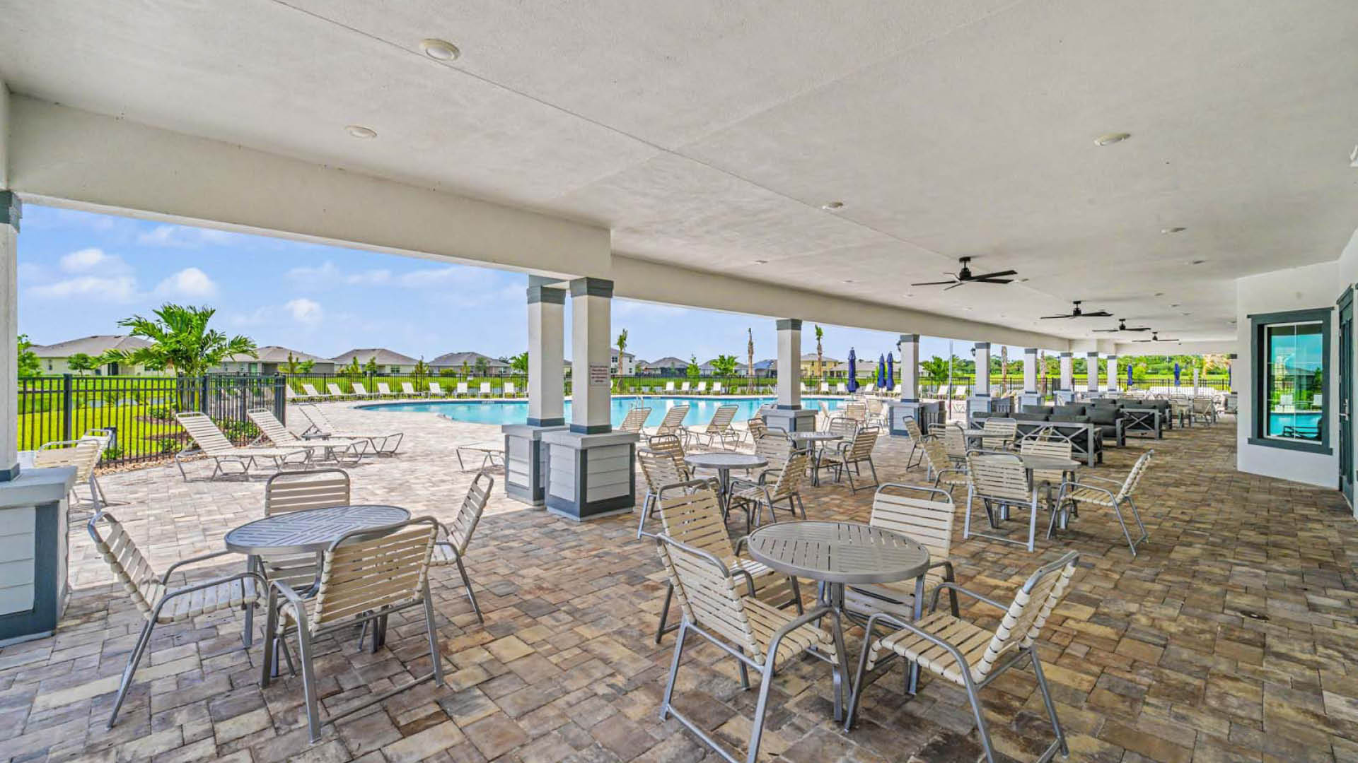 An expansive pool deck with tables and chairs, pool loungers, outdoor couches, and ceiling fans.