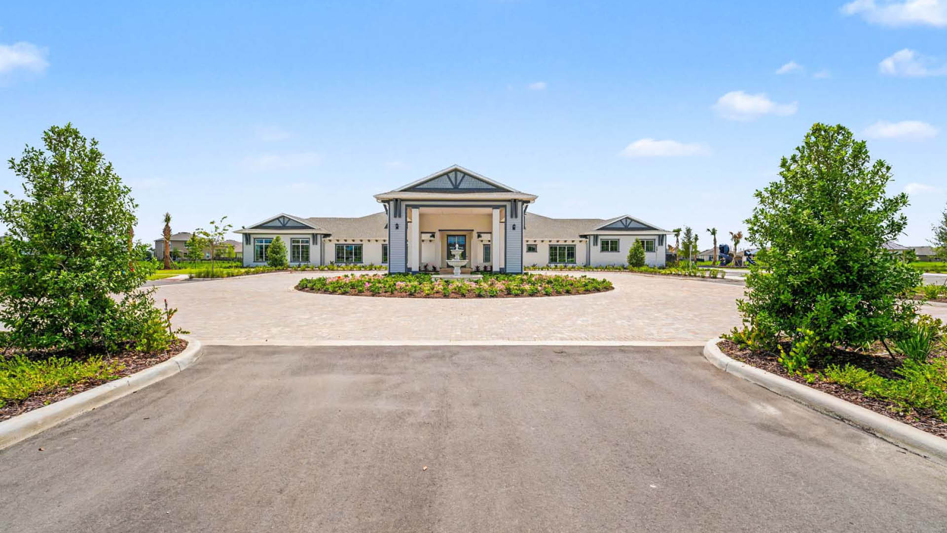 An exterior view of the front of a large clubhouse with maicured landscaping.