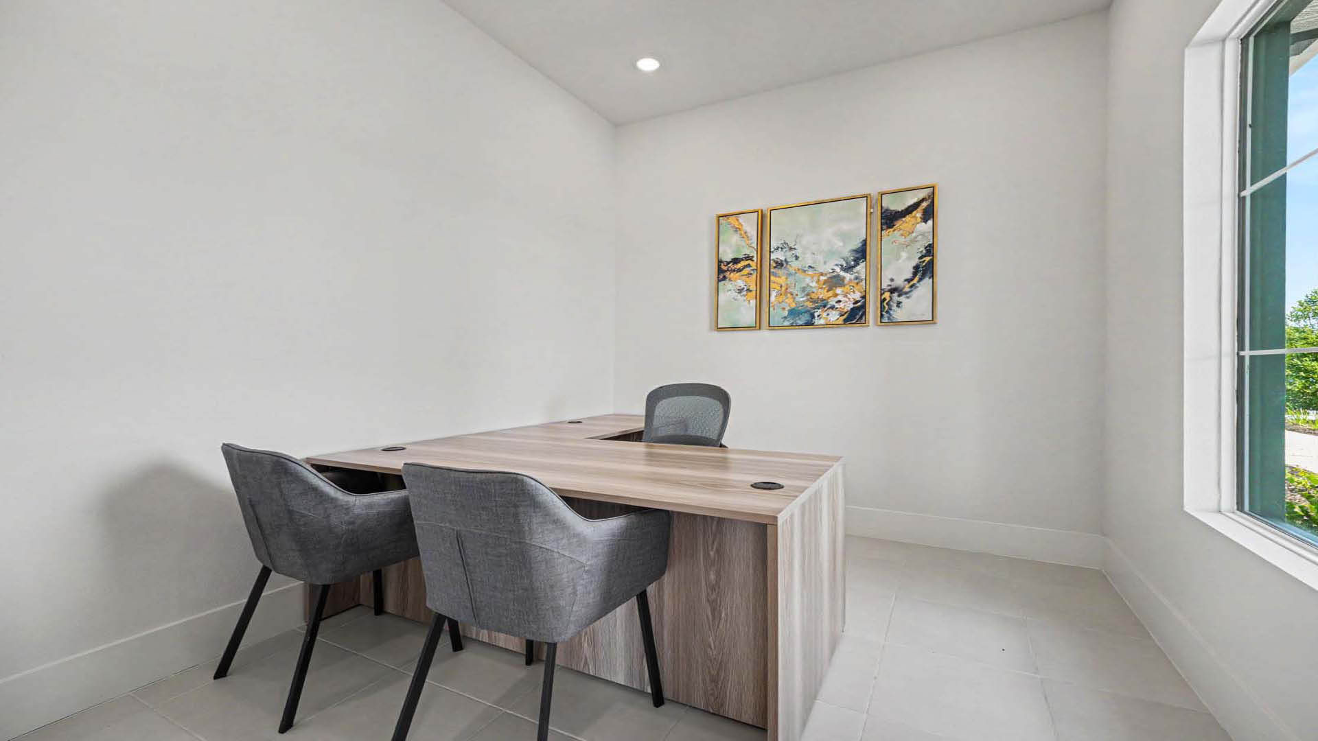 A minimal workspace with an L-shaped desk and chairs. A large window lets in natural light.