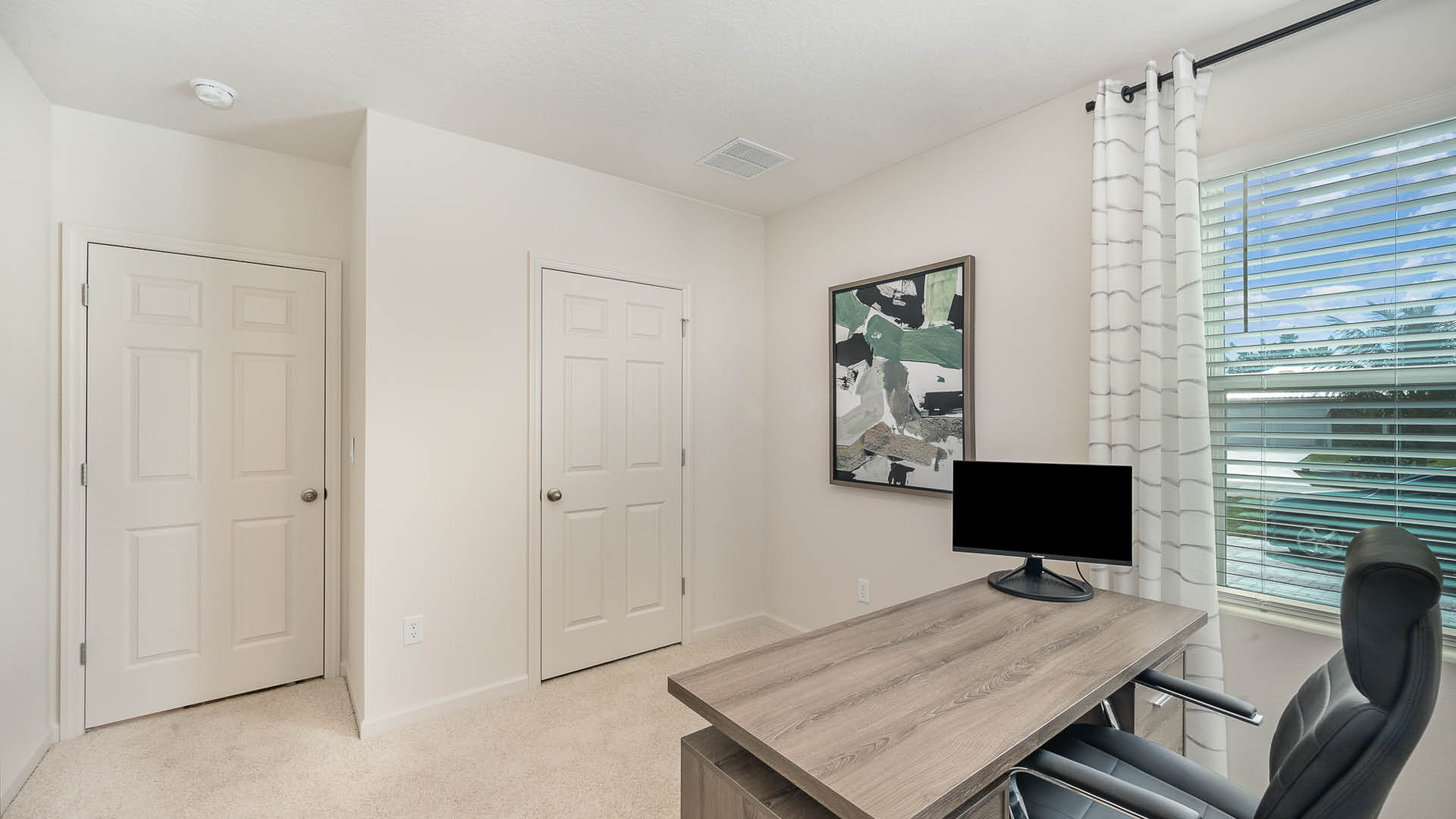 Modern office interior with a wooden desk, two upholstered chairs, a blank monitor, and abstract artwork on the wall.