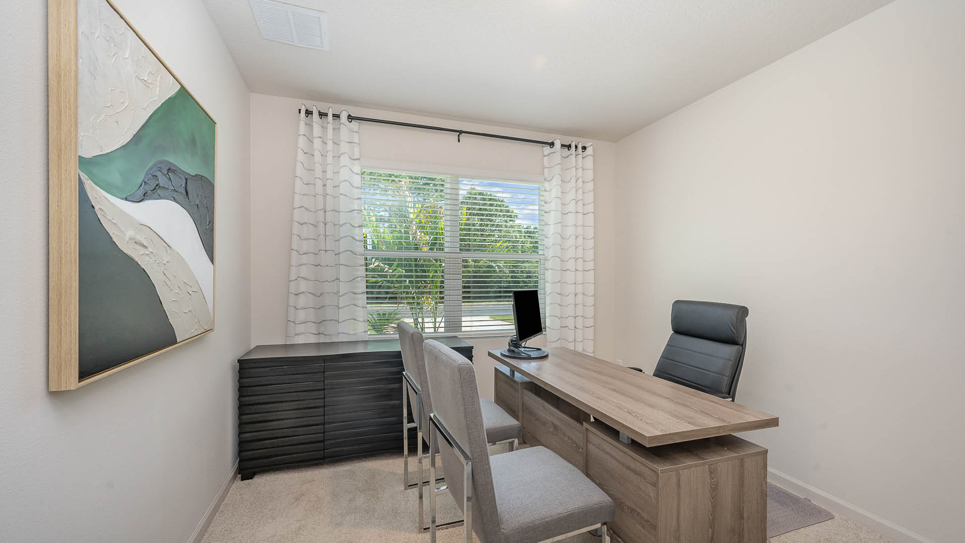 A modern home office featuring a sleek desk, ergonomic chair, two chairs, abstract art, and natural light from a window.