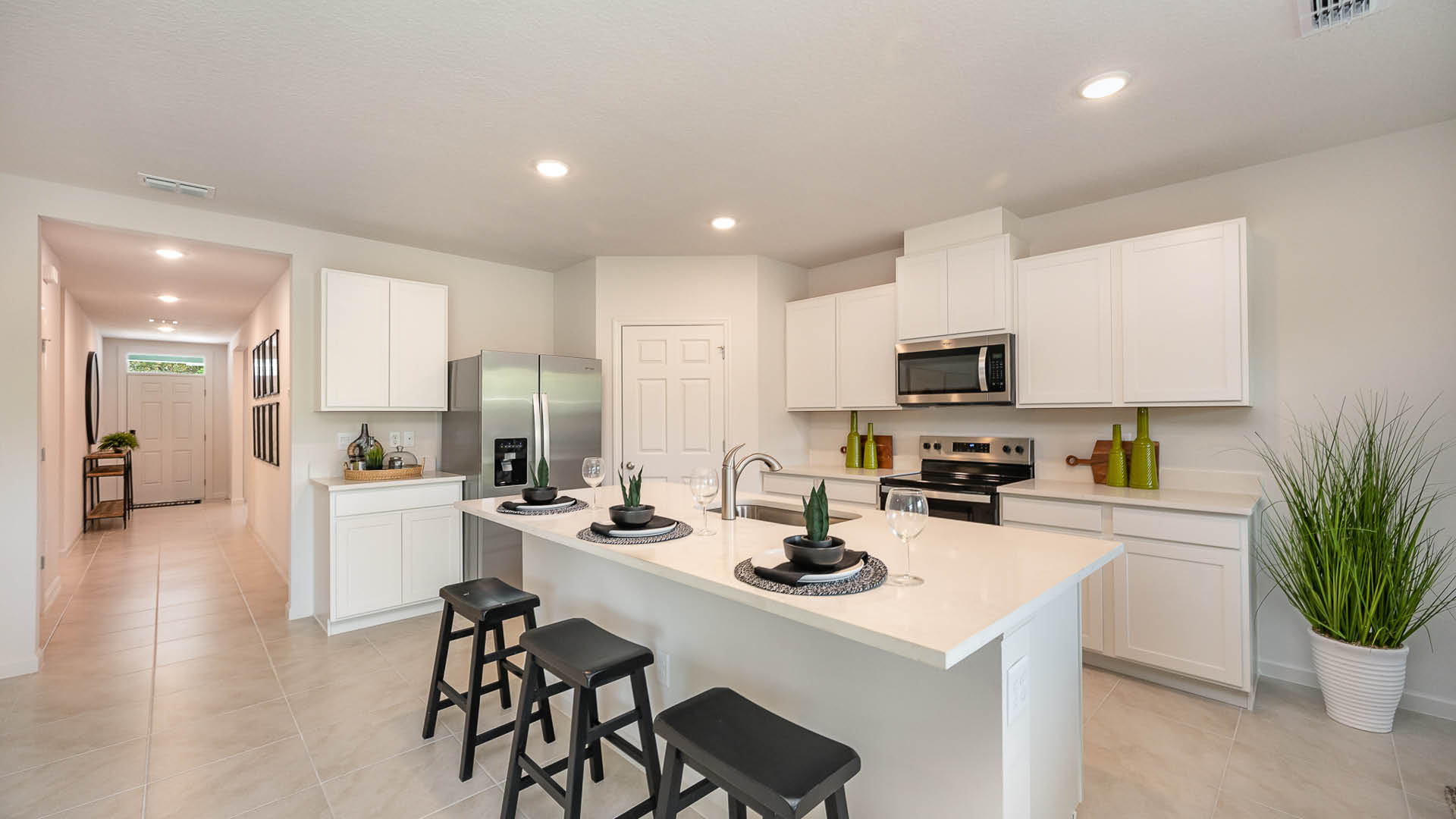 Modern kitchen featuring white cabinetry, stainless steel appliances, a large quartz countertop, and ample natural light from nearby windows.