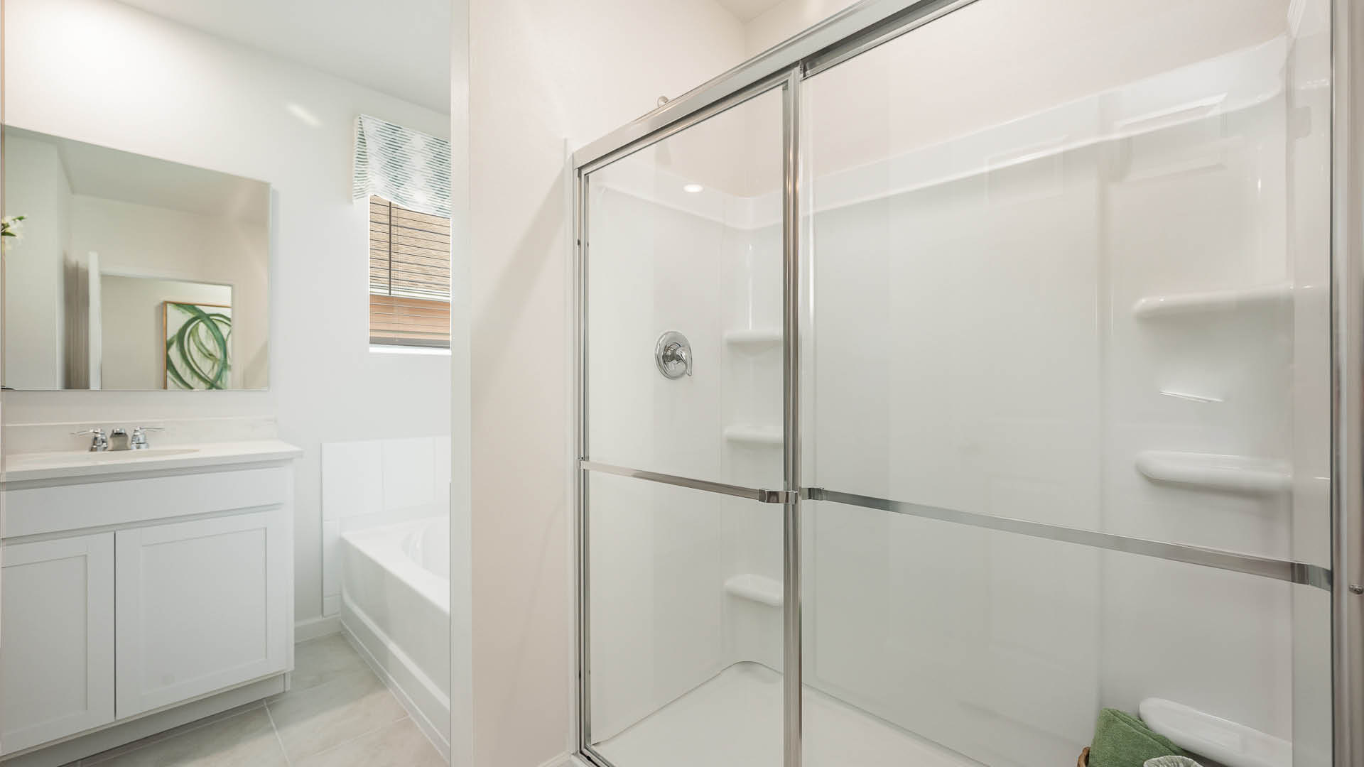 Bright modern bathroom featuring a glass shower, white cabinetry, and a bathtub, with natural light from a nearby window.