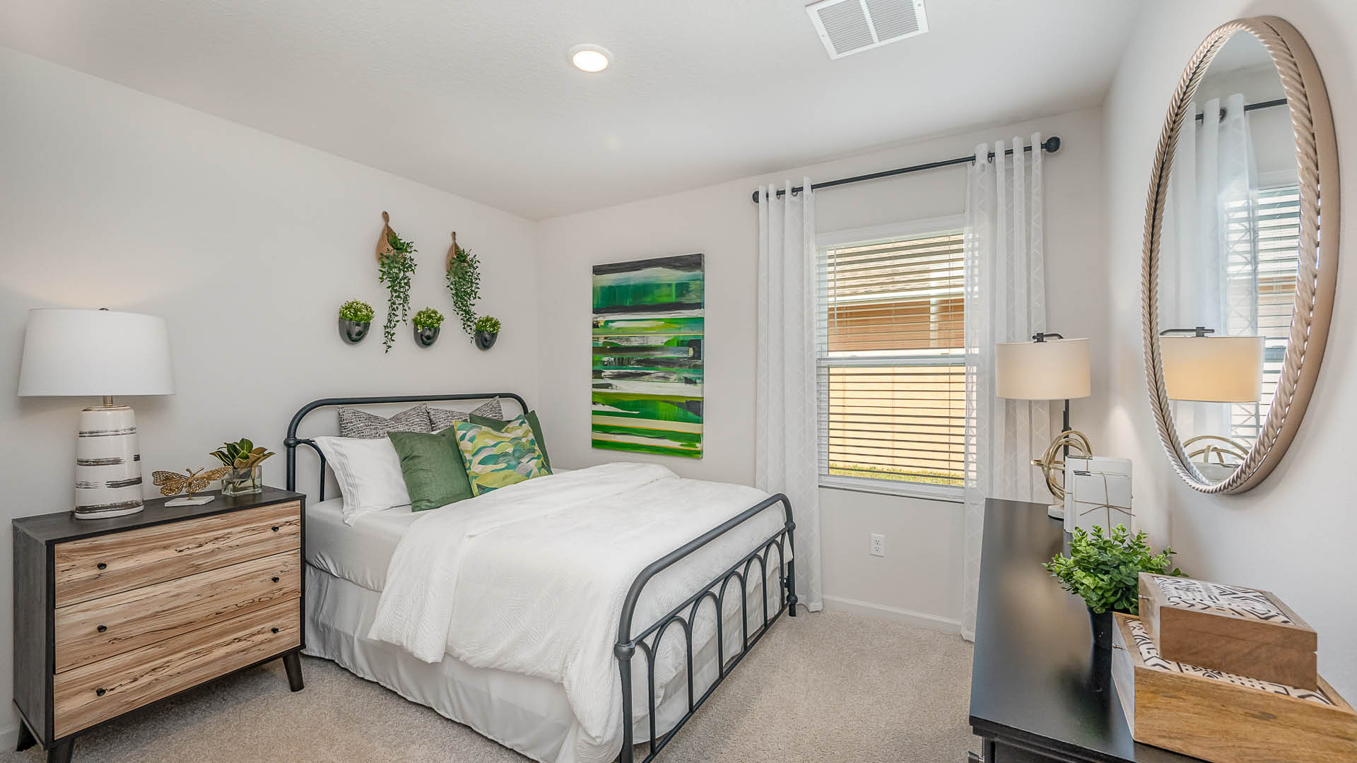 Cozy bedroom featuring a metal bed frame, colorful pillows, patterned art, and decorative plants, with soft lighting and draped curtains.