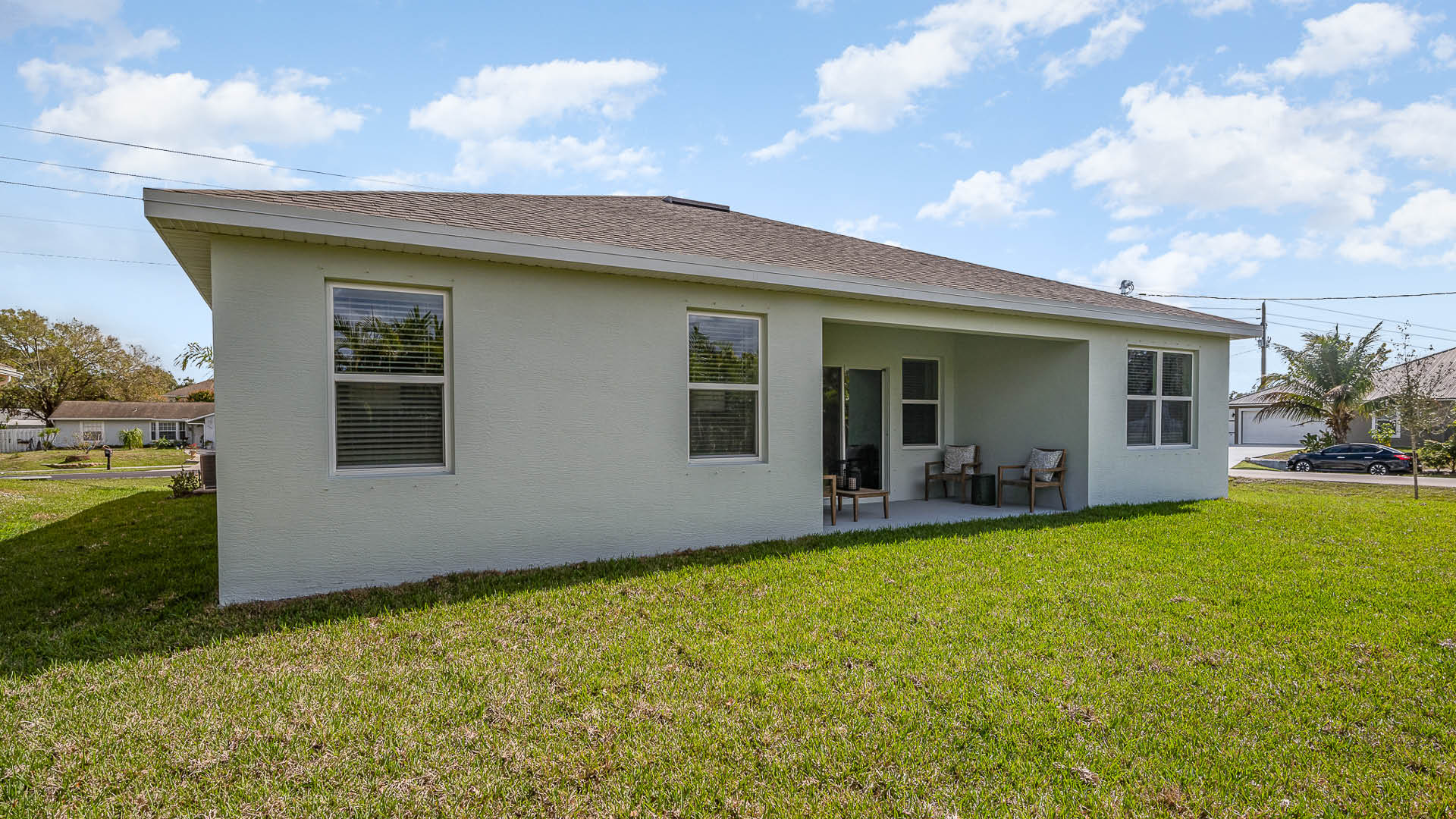 A view of a light-colored house with a covered porch, surrounded by a grassy lawn under a partly cloudy sky.