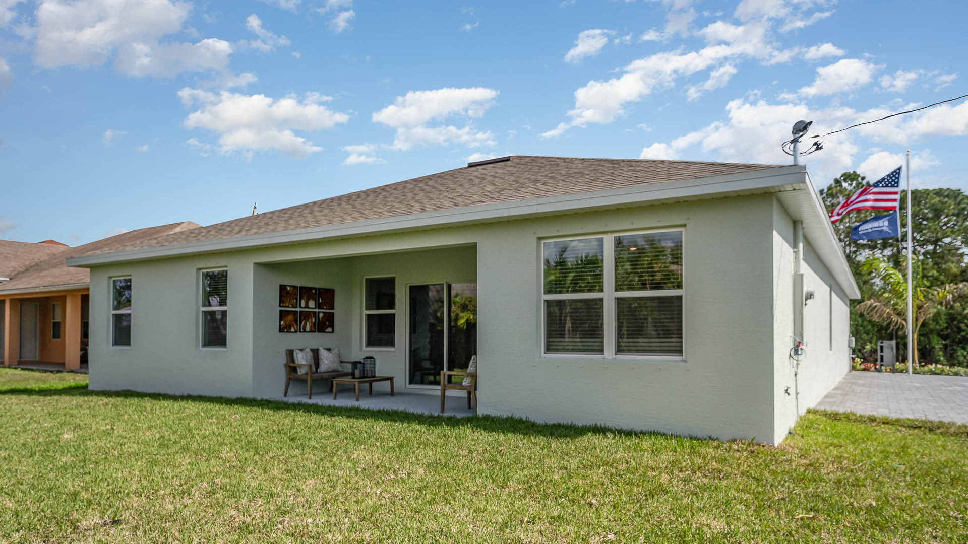 A view of a light-colored house with a covered porch, surrounded by a grassy lawn under a partly cloudy sky.