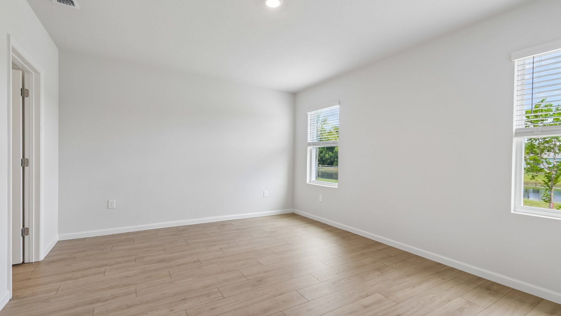 A large bedroom with windows, allowing natural light to illuminate the space. There is an open door to a large ensuite bathroom.