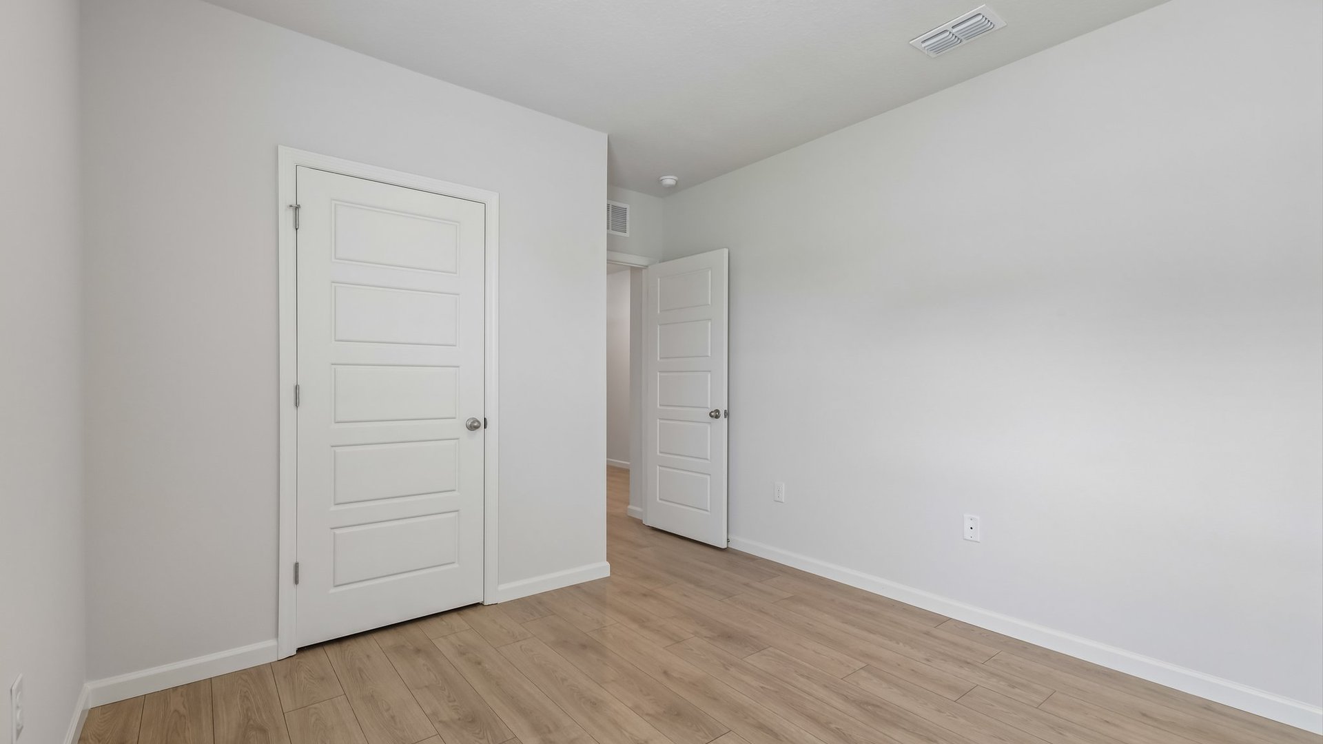 An empty room with a window, allowing natural light to illuminate the space. The open door to the room and a closed closet door are visible.