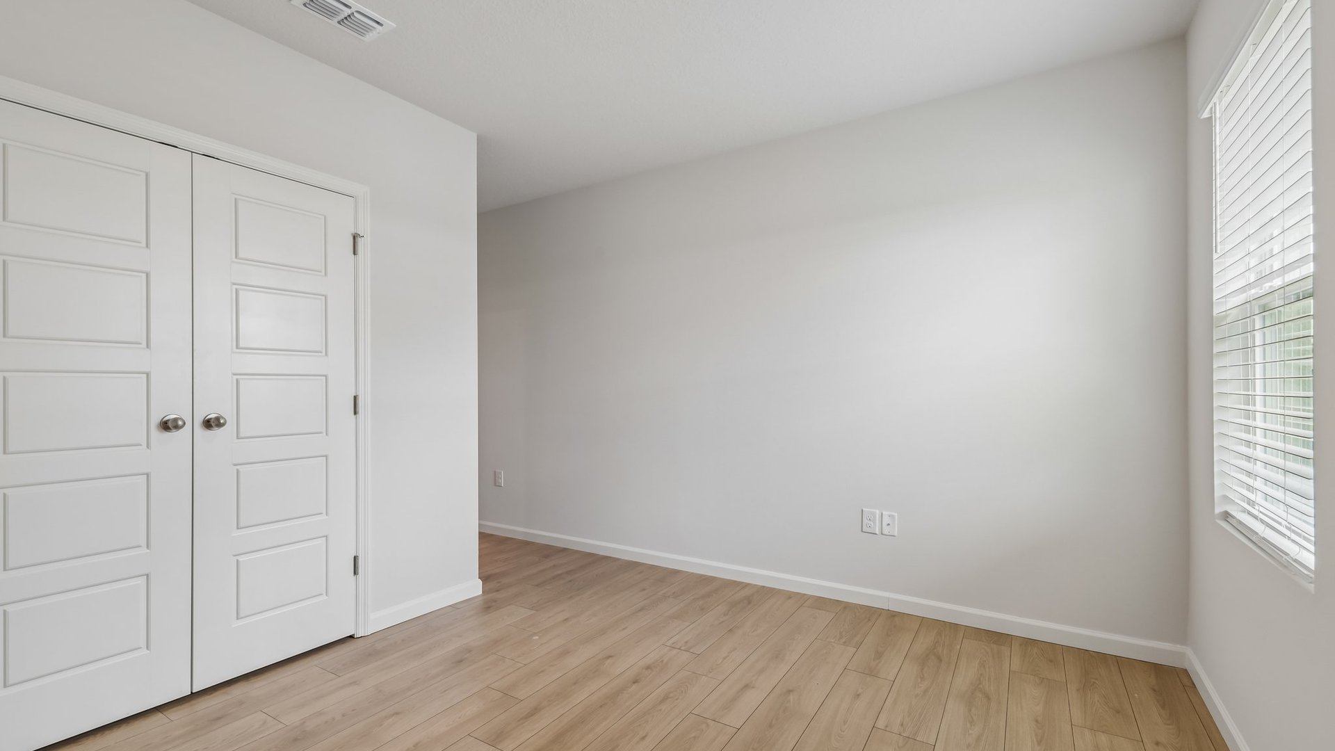 An empty room with a window and double door closet.