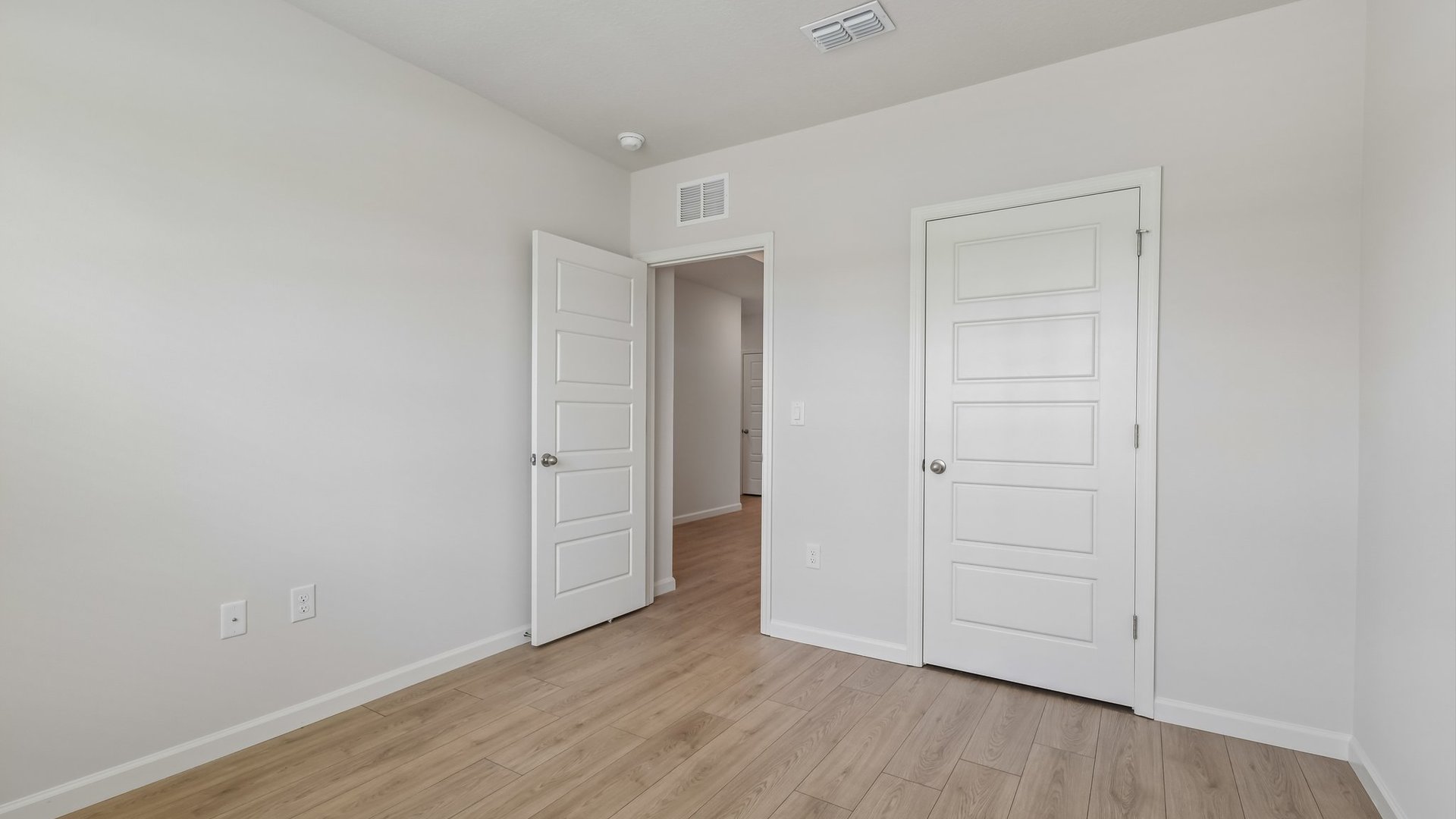 An empty room with a window, allowing natural light to illuminate the space. The open door to the room and a closed closet door are visible.