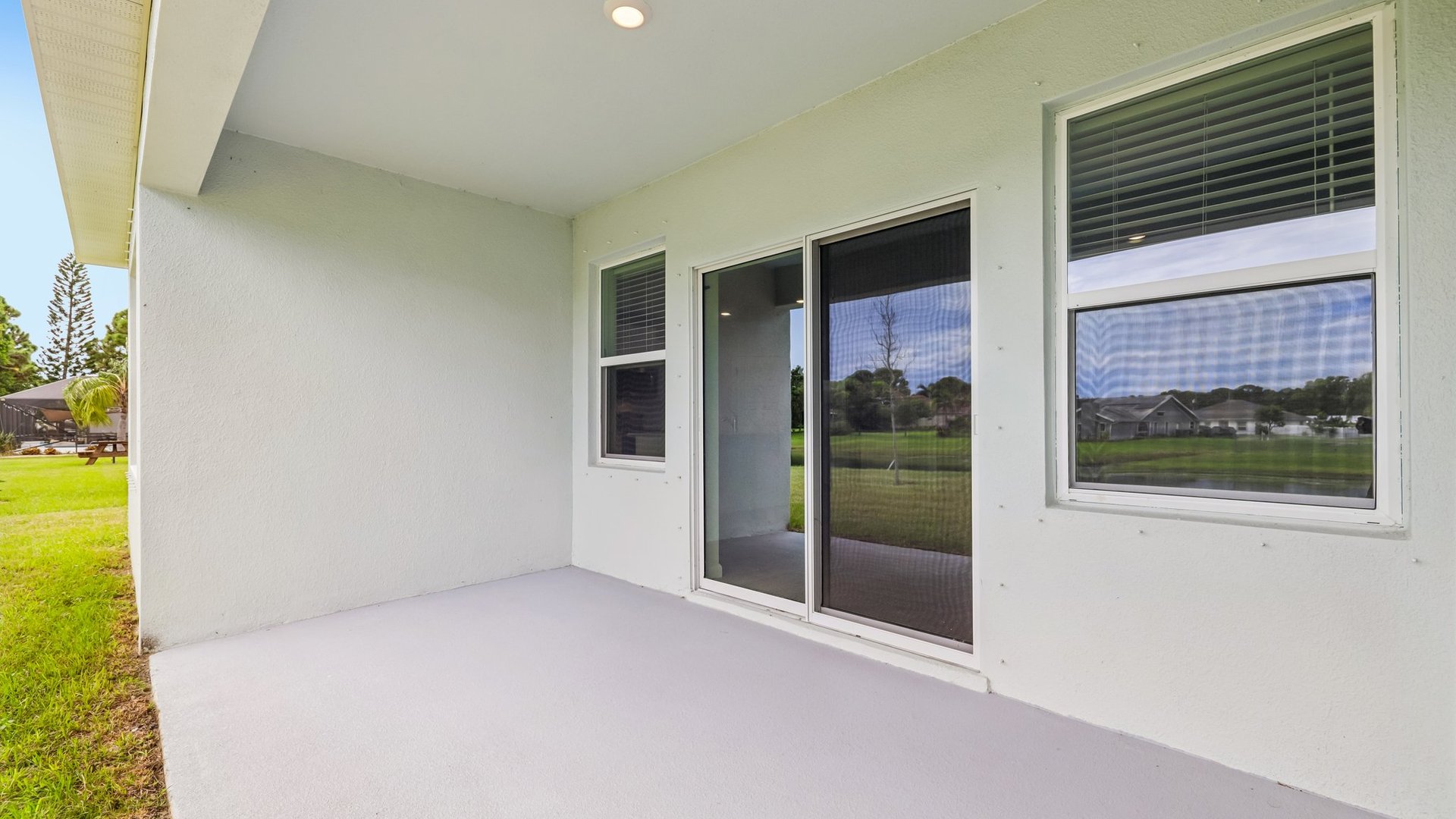 A rear view of a house featuring a stucco exterior, sliding glass door, and a covered patio.