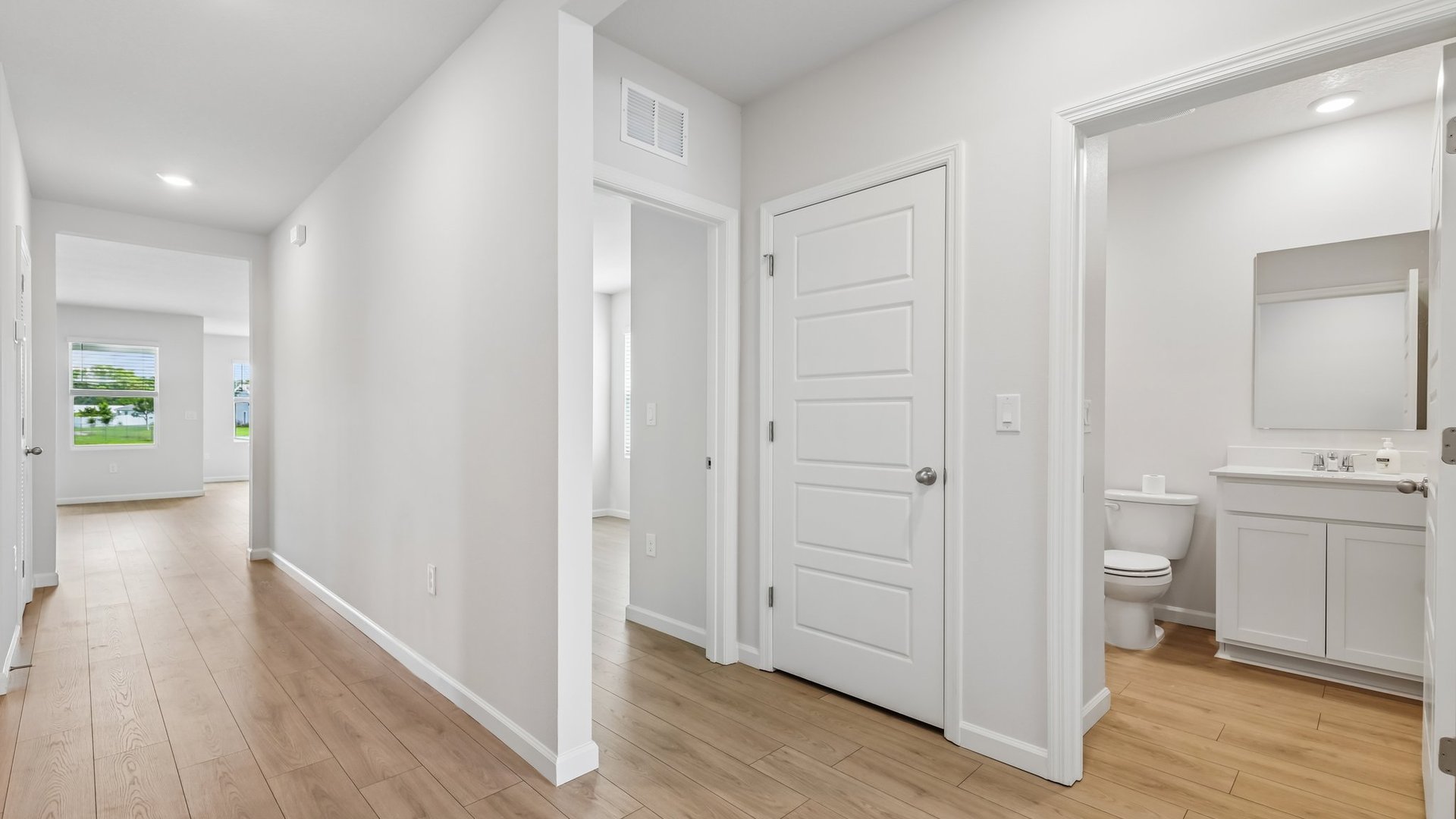 A bright entryway hallway with an open door to a modern bathroom and several doors leading elsewhere.