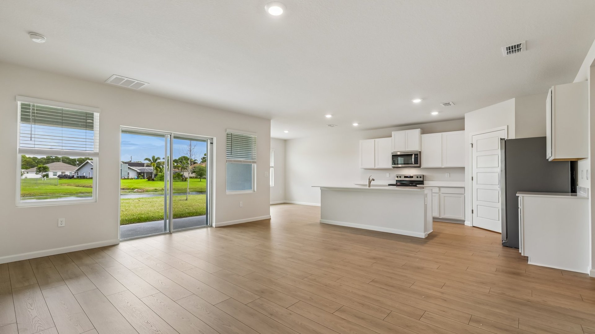 A spacious room, with a view of a kitchen and dining area. There are several windows and sliding glass doors leading to a covered patio.