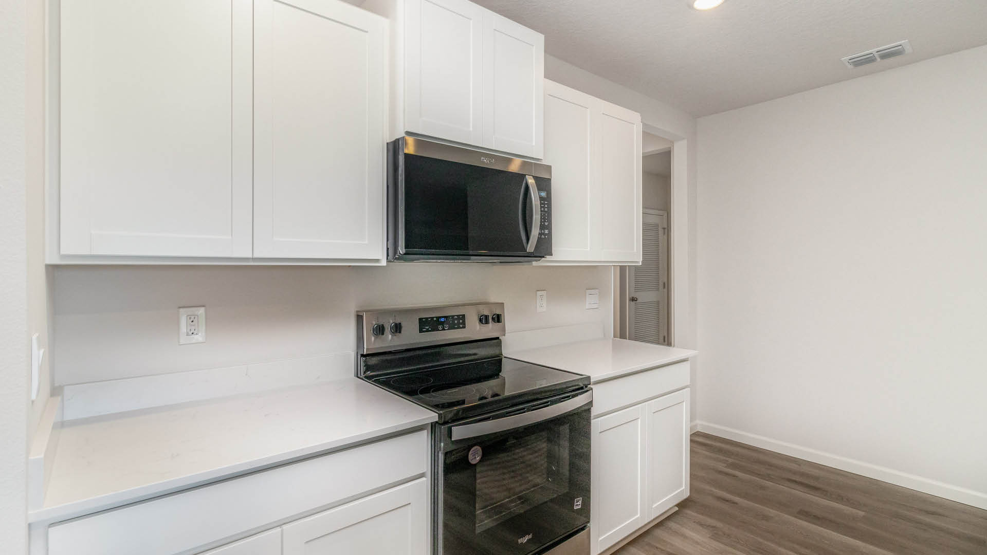 A large kitchen with quartz countertops, stainless steel appliances, and an opening to other areas to the side.