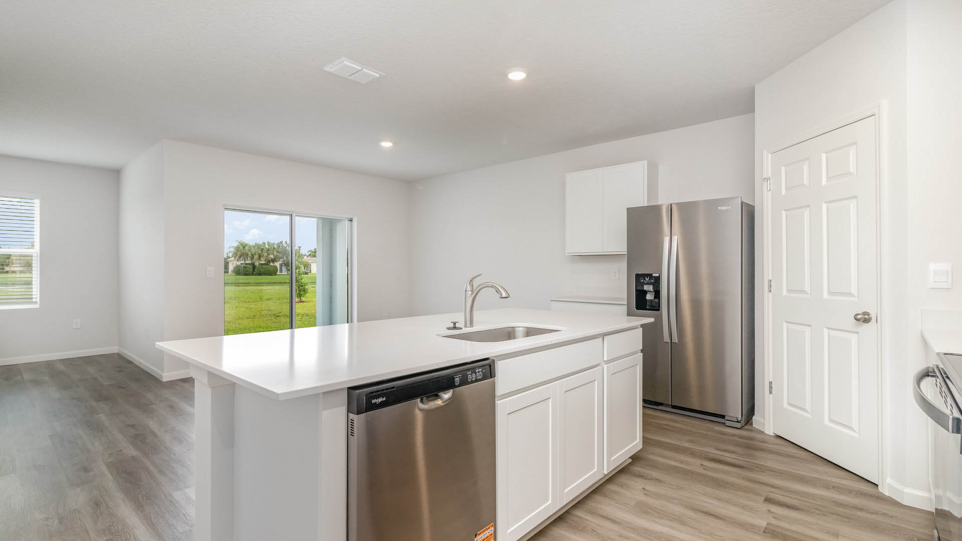 A large kitchen with quartz countertops, stainless steel appliances, and an island. A dining area featuring large windows and a sliding glass door are visible.