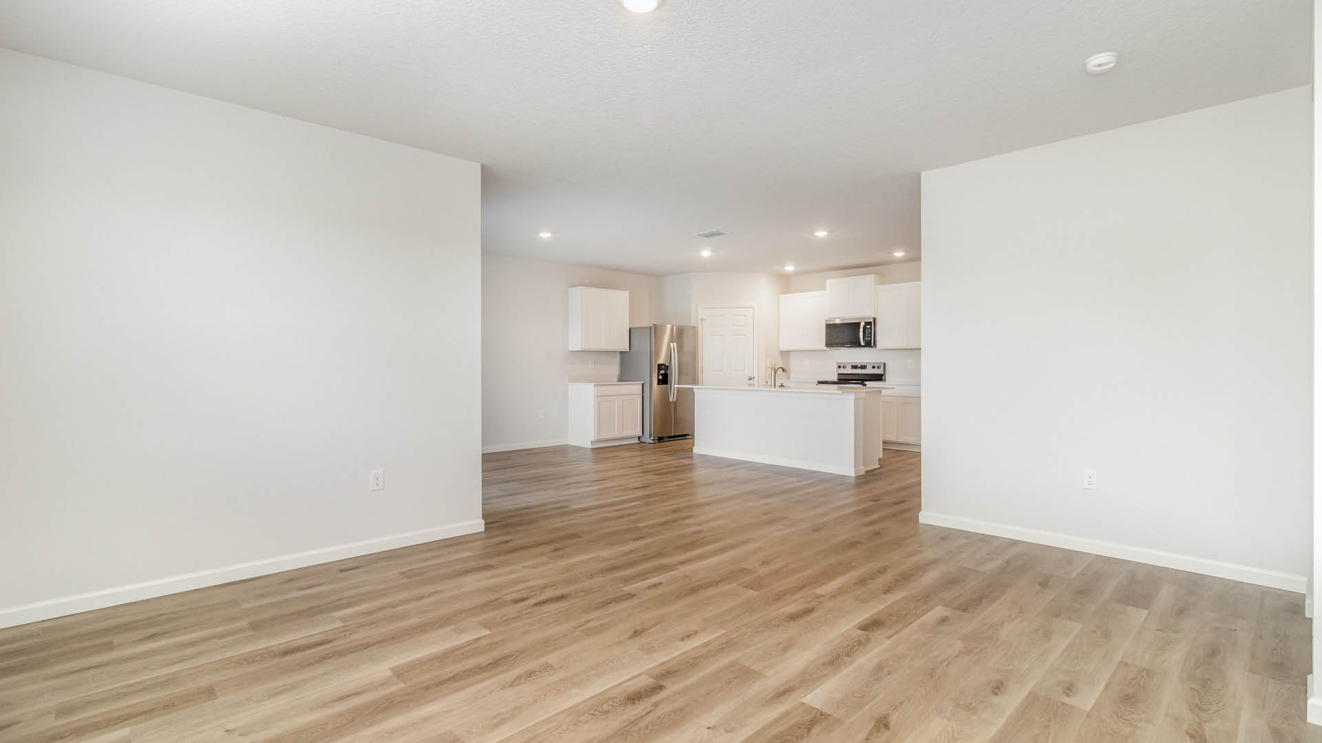 A spacious room, with a view of a kitchen area and Mohawk® Revwood Select Plank Flooring throughout.
