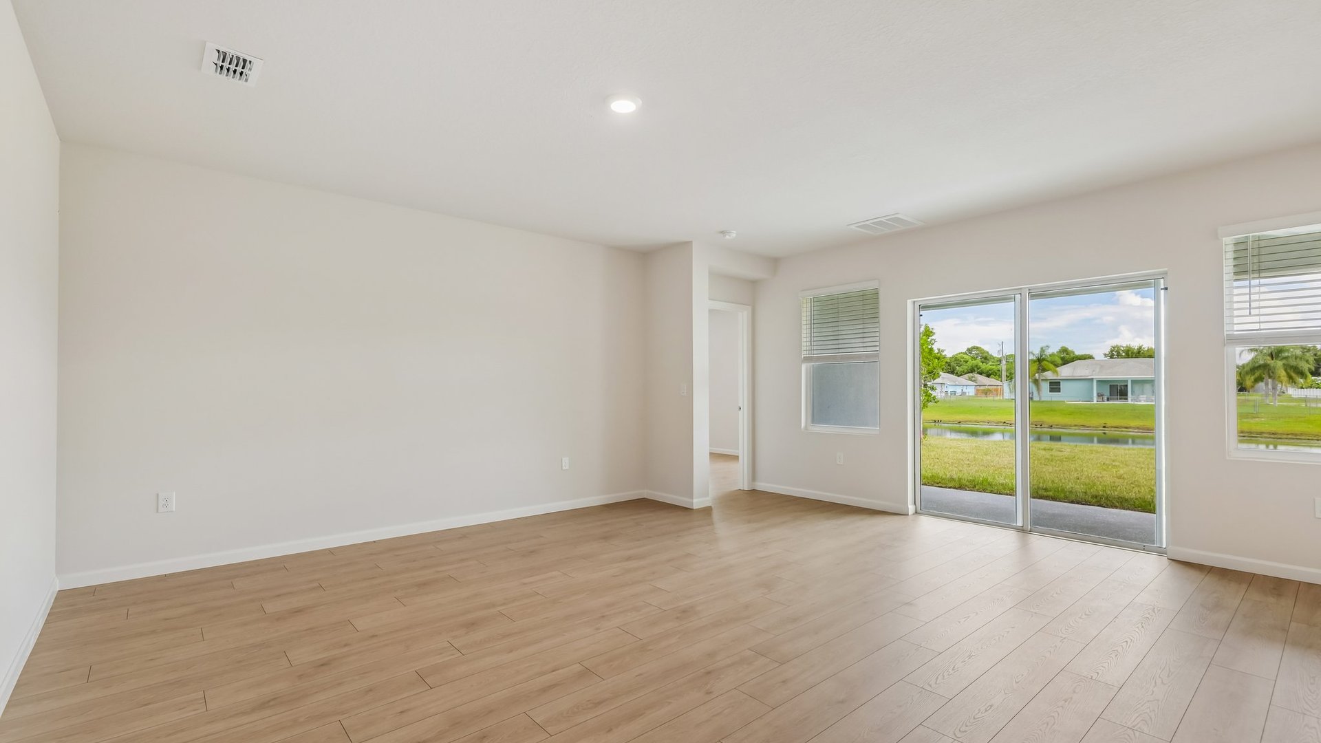A spacious, empty living room with large windows and sliding glass doors leading to a covered patio. An open door leading to another room is visible.
