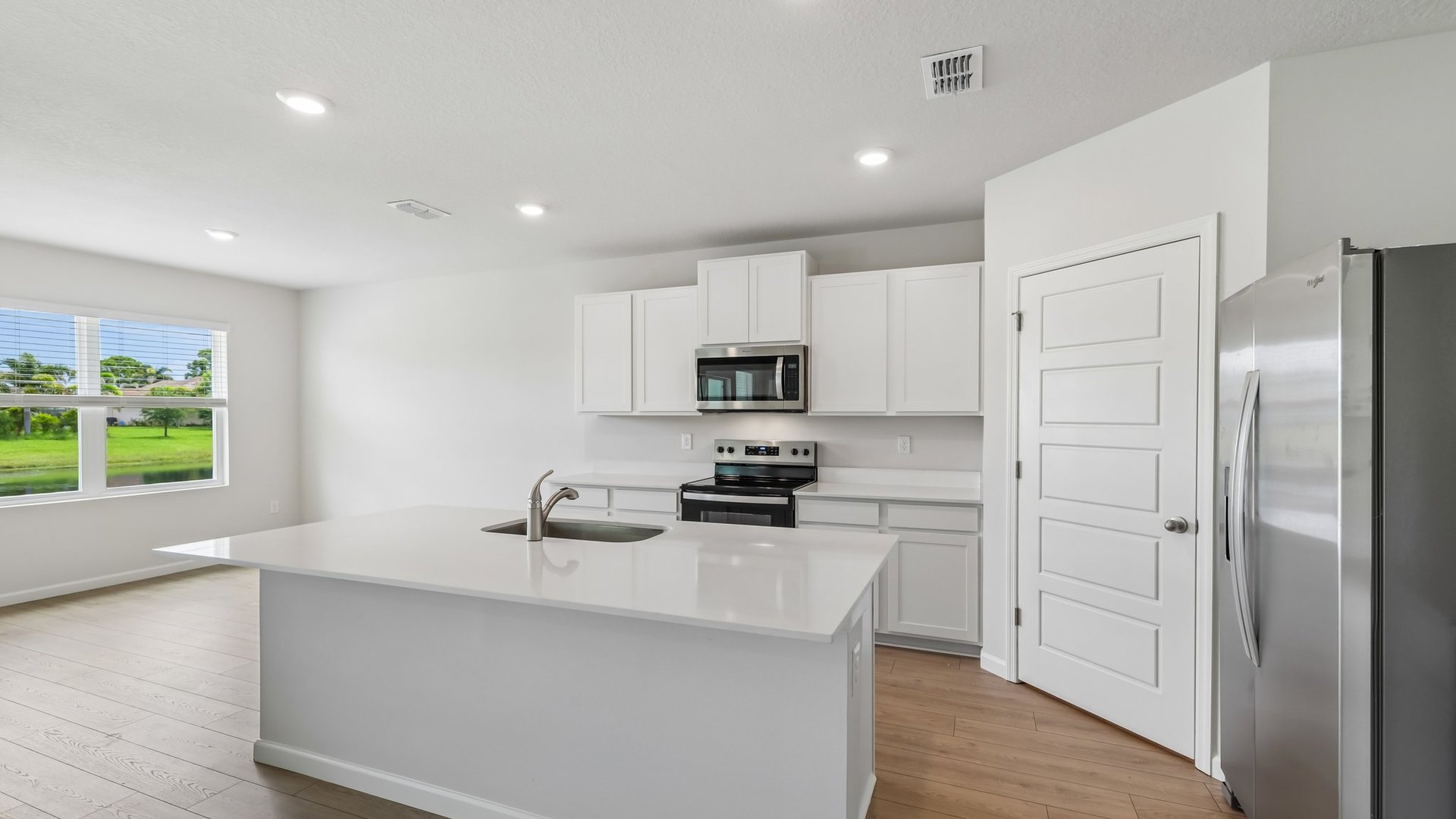 A large kitchen with quartz countertops, stainless steel appliances, and an island with room for seating. A dining area featuring a large window is visible.