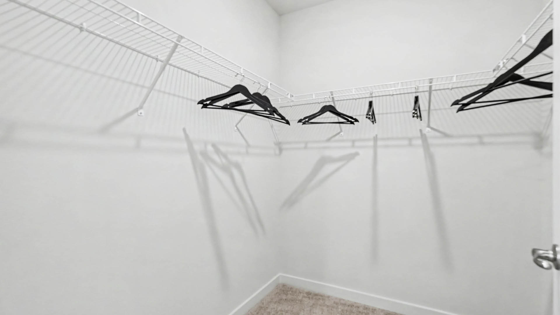 A large walk-in closet with several black hangers hanging on white wire shelves and racks.