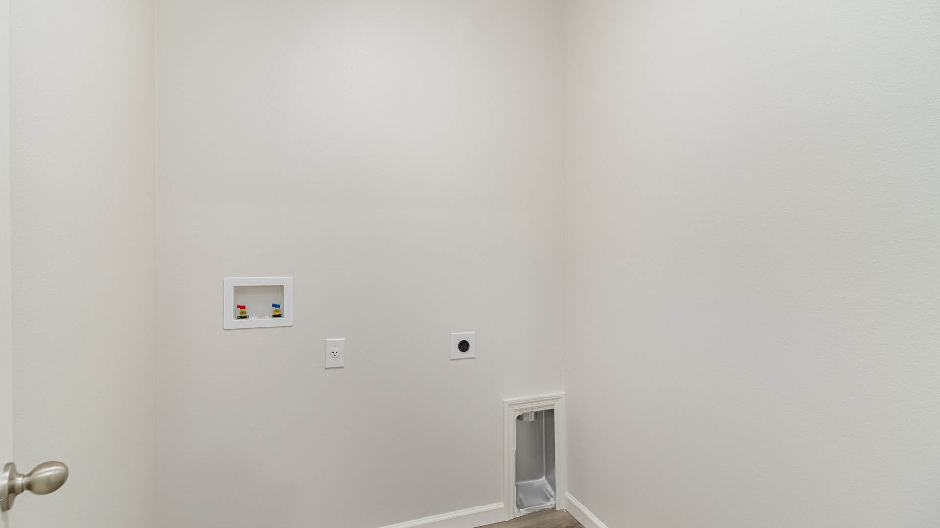 20. A small laundry room with light-colored walls, tiled floor, and utility connections on one wall, featuring a closed door on the left.