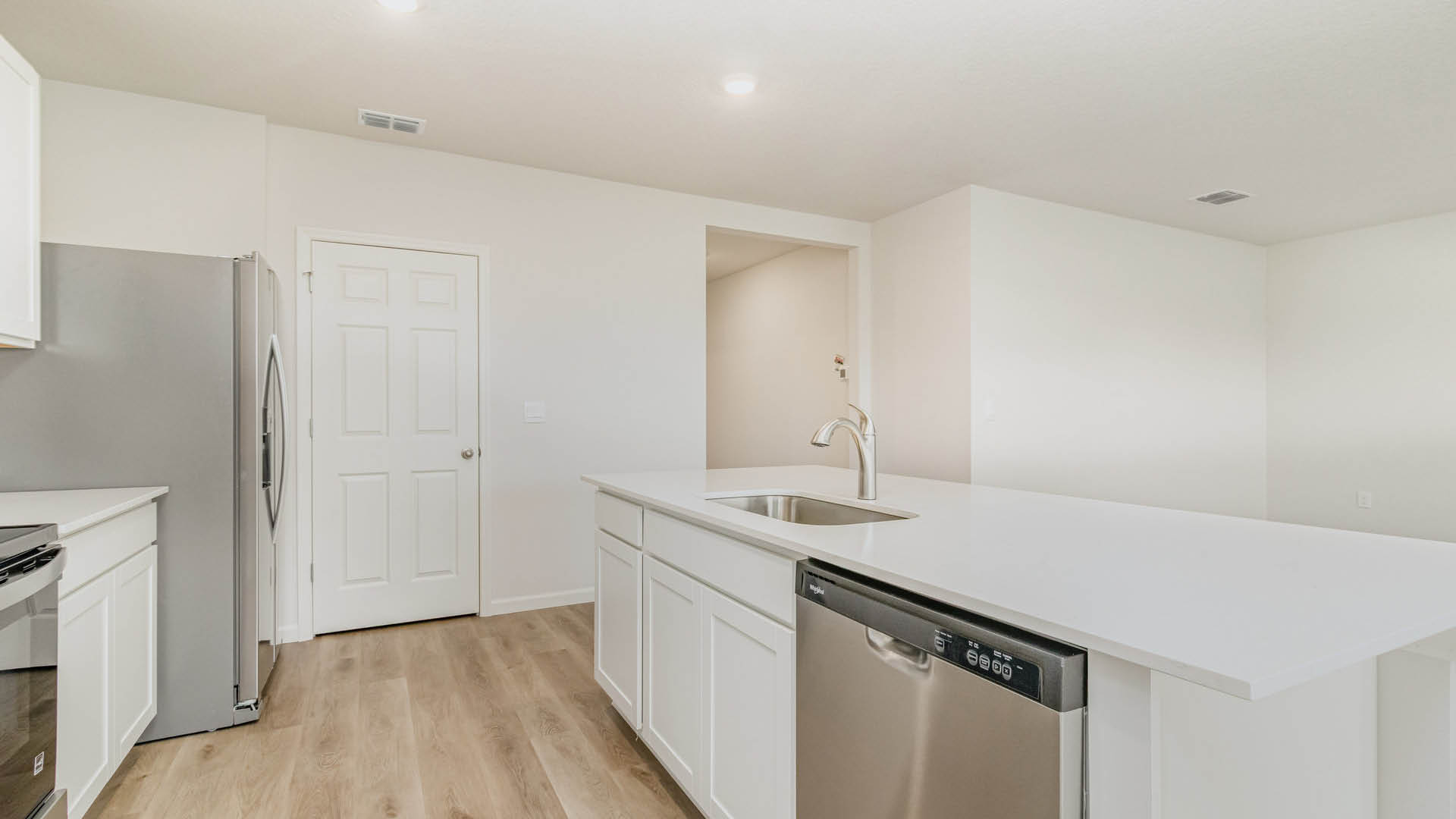 A modern kitchen features white walls and cabinetry, a central island with a built-in sink and stainless steel dishwasher, and a matching refrigerator and stove against the wall.