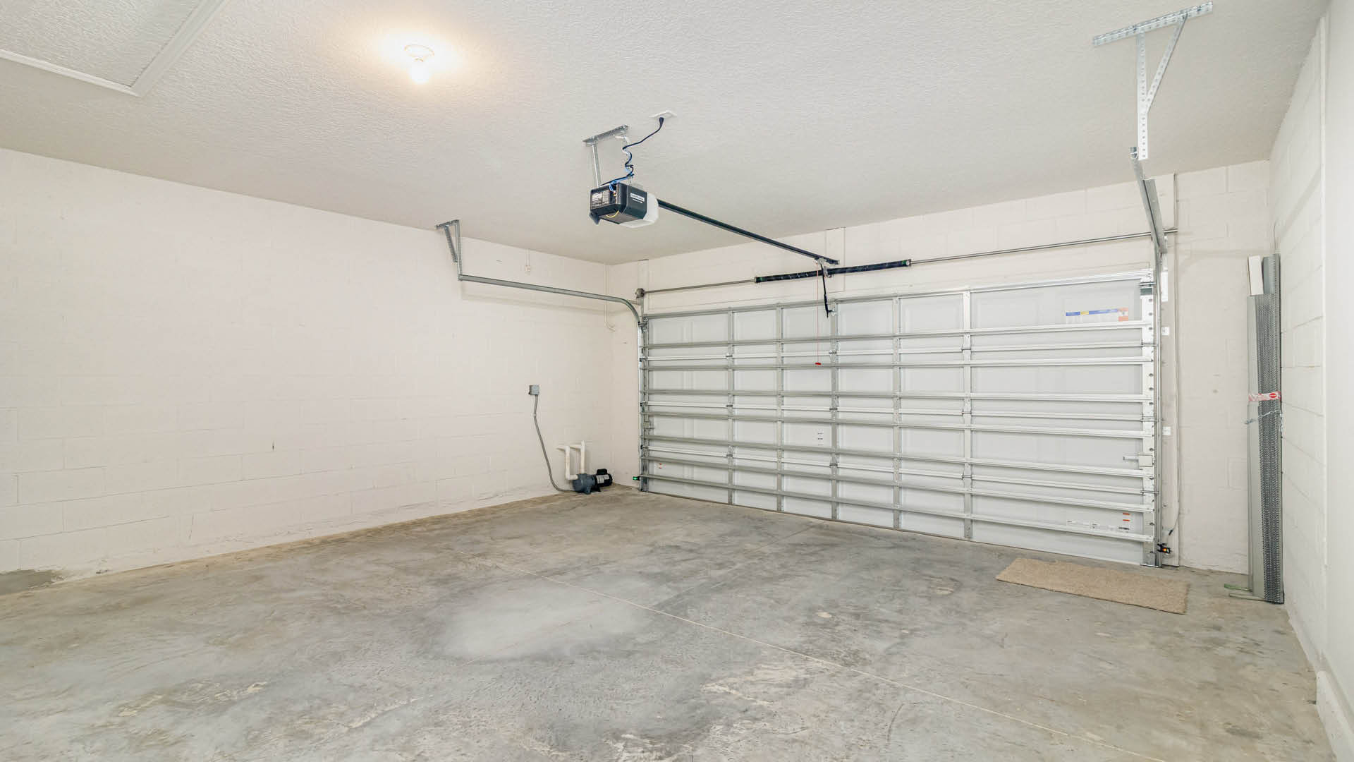 A spacious, clean garage with concrete flooring, a garage door, and electrical panel along a white cinder block wall.